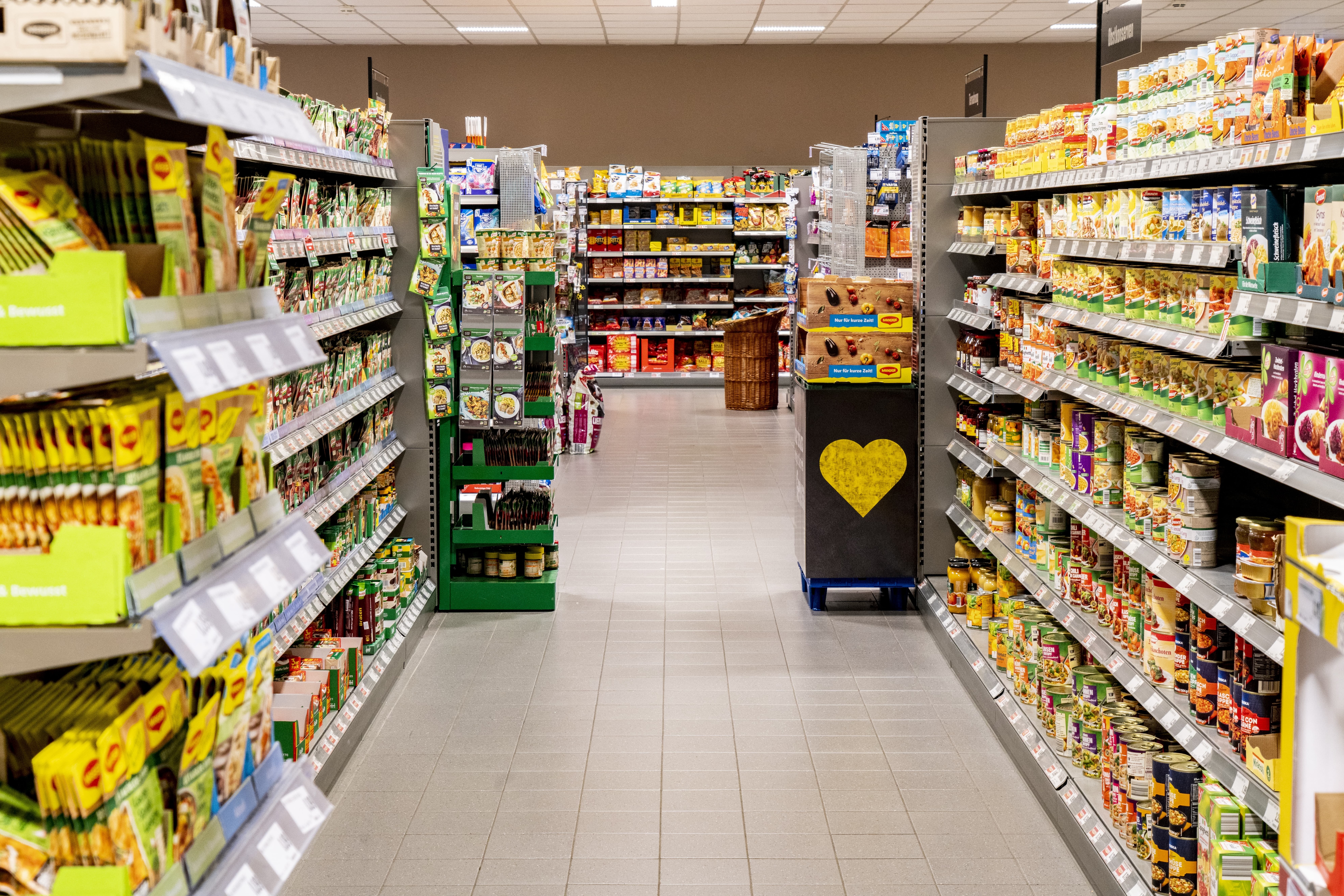 Gang eines EDEKA-Markts, rechts stehen Regale mit Konservengerichten, links befinden sich Fertigsuppen in Tüten.