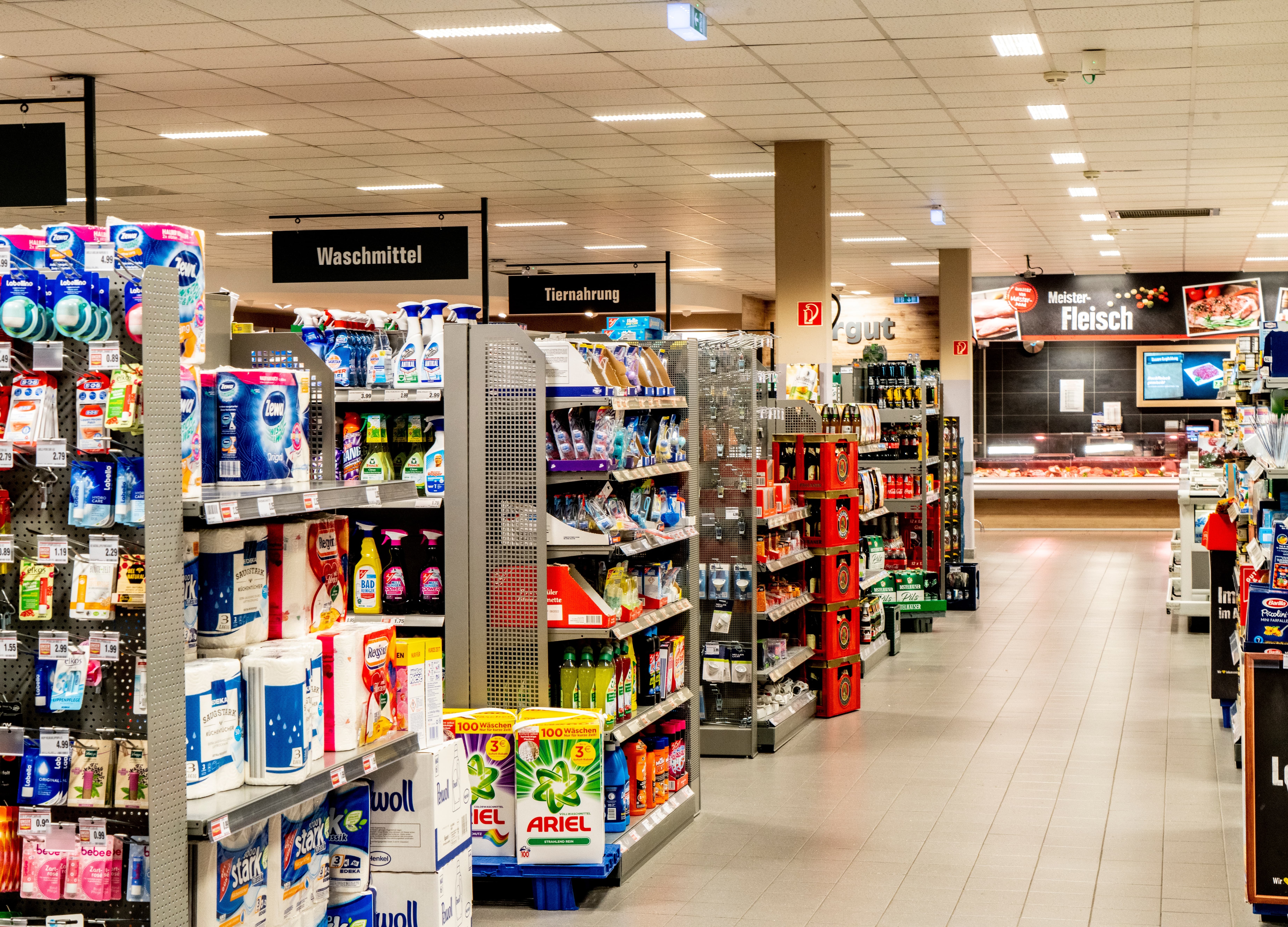 Gänge eines EDEKA-Markts, die sich nach links öffnen. Zu sehen sind unter anderem Waschmittel und Tiernahrung.
