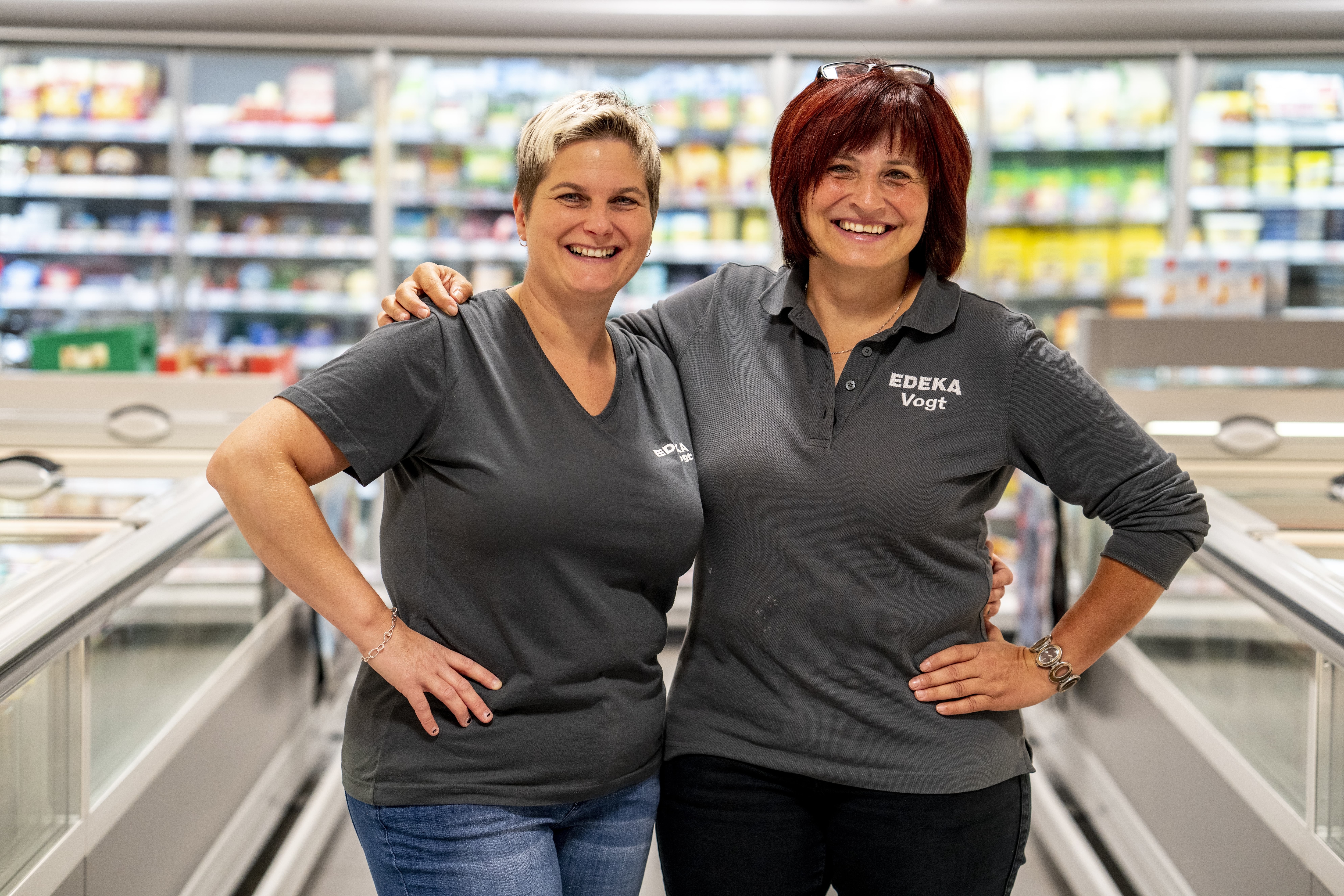 Zwei Mitarbeiterinnen stehen Arm in Arm und lächeln in die Kamera, im Hintergrund Produktregale.