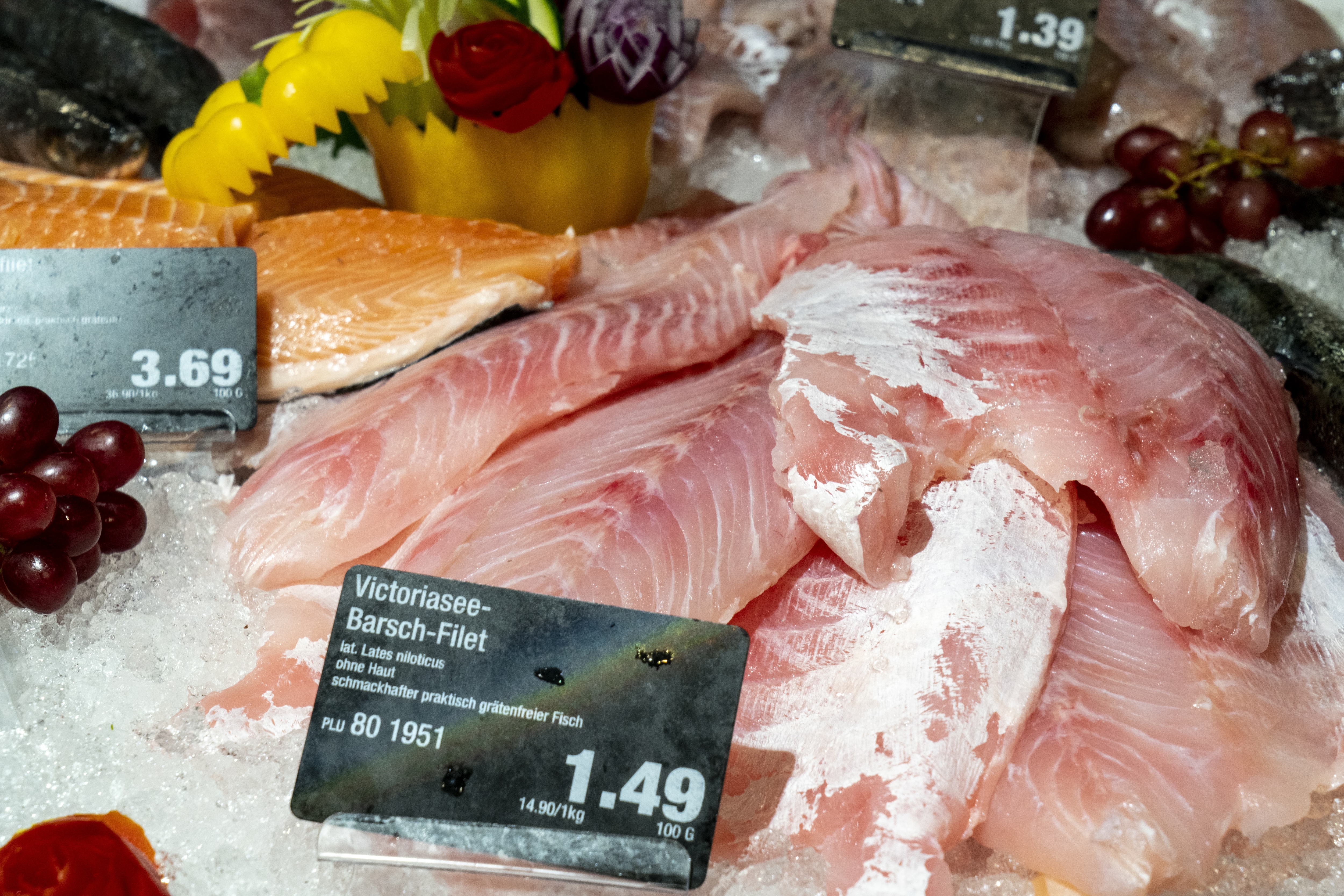 Fisch in einer Auslage im Close-Up, mit Preisschildern und Obst als Deko.