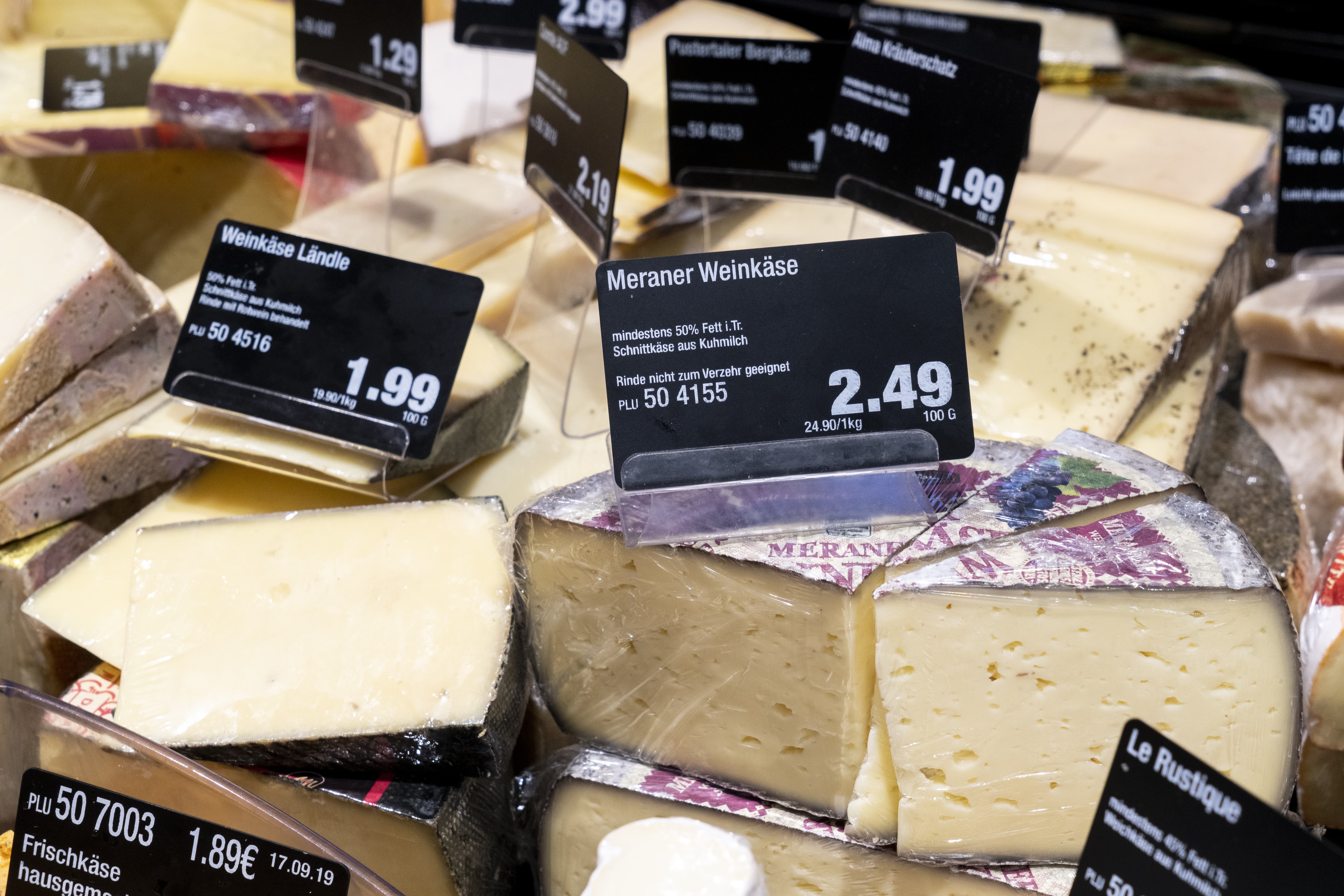 Käseauslage einer Bedienungstheke mit vielen verschiedenen Käsesorten und Preisschildern.