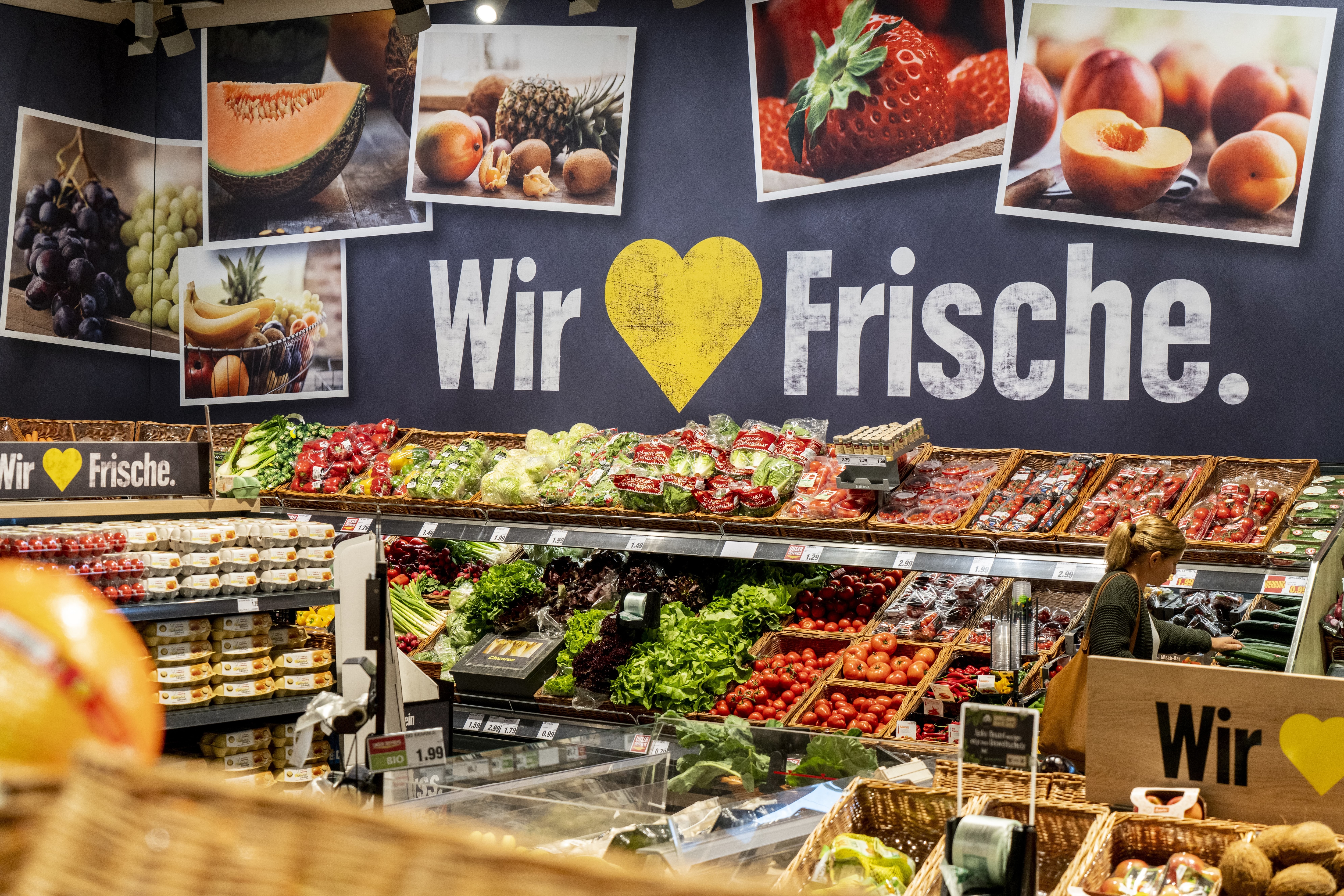 Die Obst- und Gemüseabteilung eines EDEKA-Markts. Über einem Obstregal steht groß gedruckt: Wr lieben Frische.