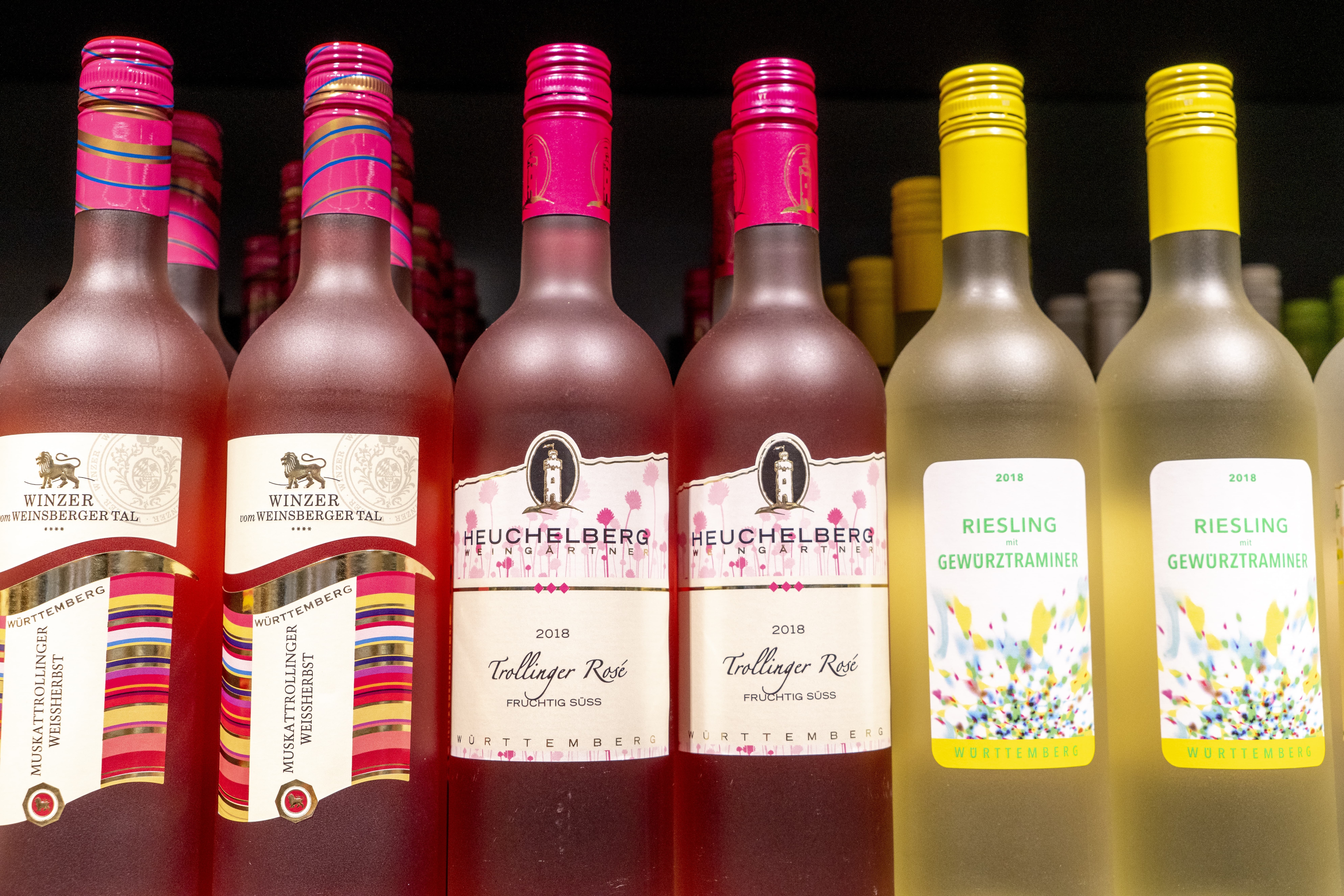 Mehrere Weinflaschen mit pinken und gelben Deckeln in einem Regal.