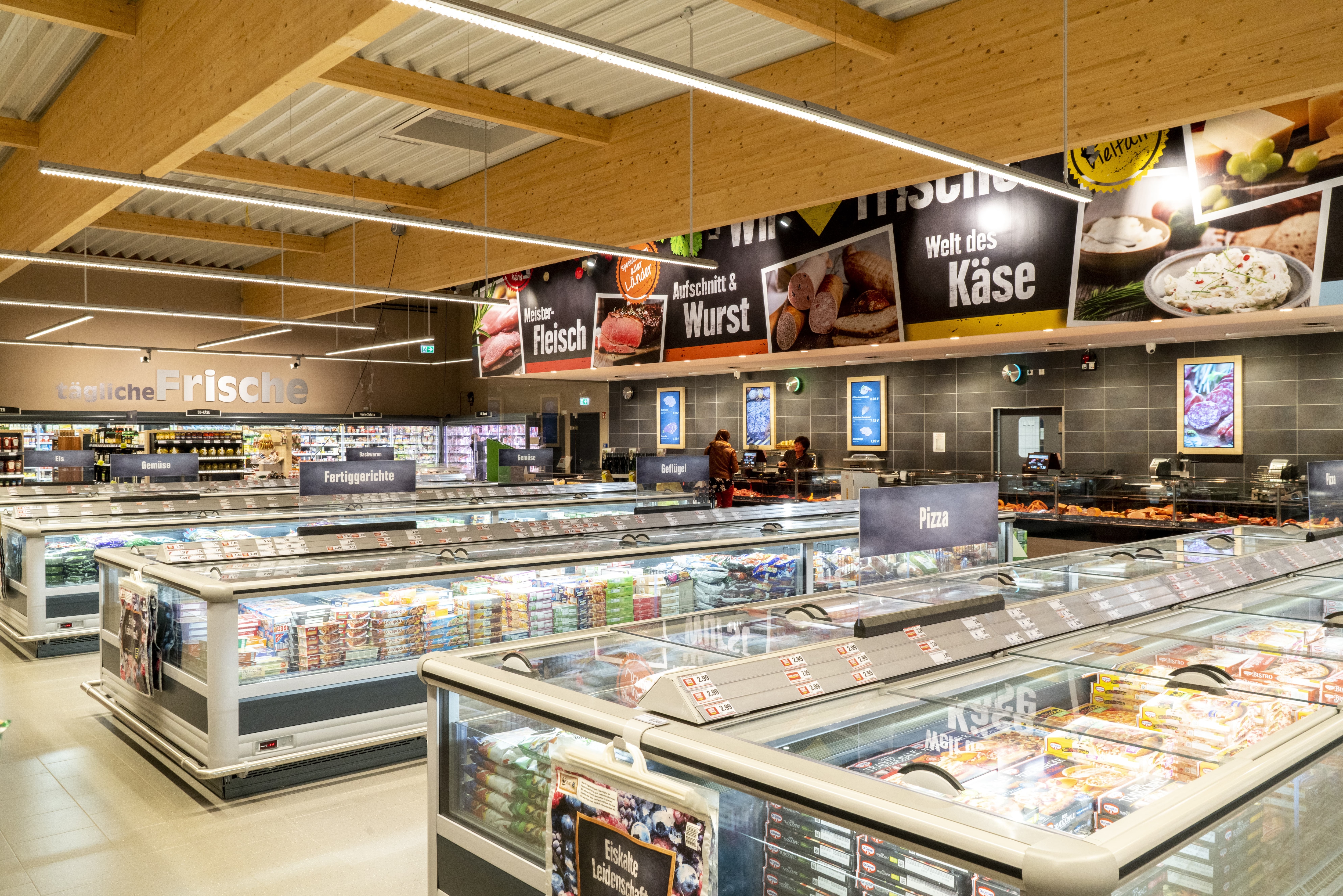 Tiefkühltruhen mit Tiefkühlpizzen im Vordergrund, dahinter die Bedientheke des Markts.