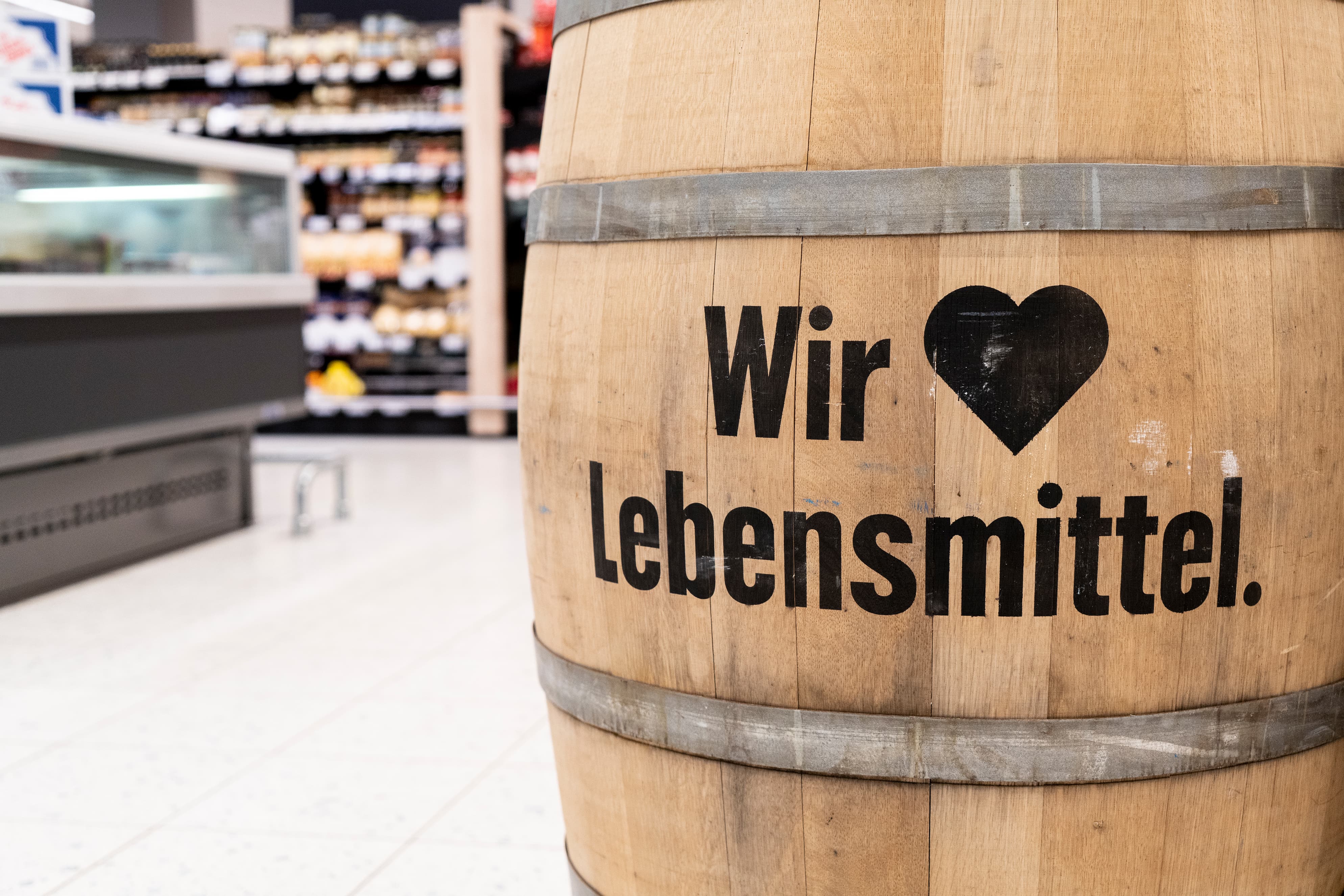 Ein Fass, auf dem steht: Wir lieben Lebensmittel. Im Hintergrund die Tiefkühltheke eines EDEKA-Markts.