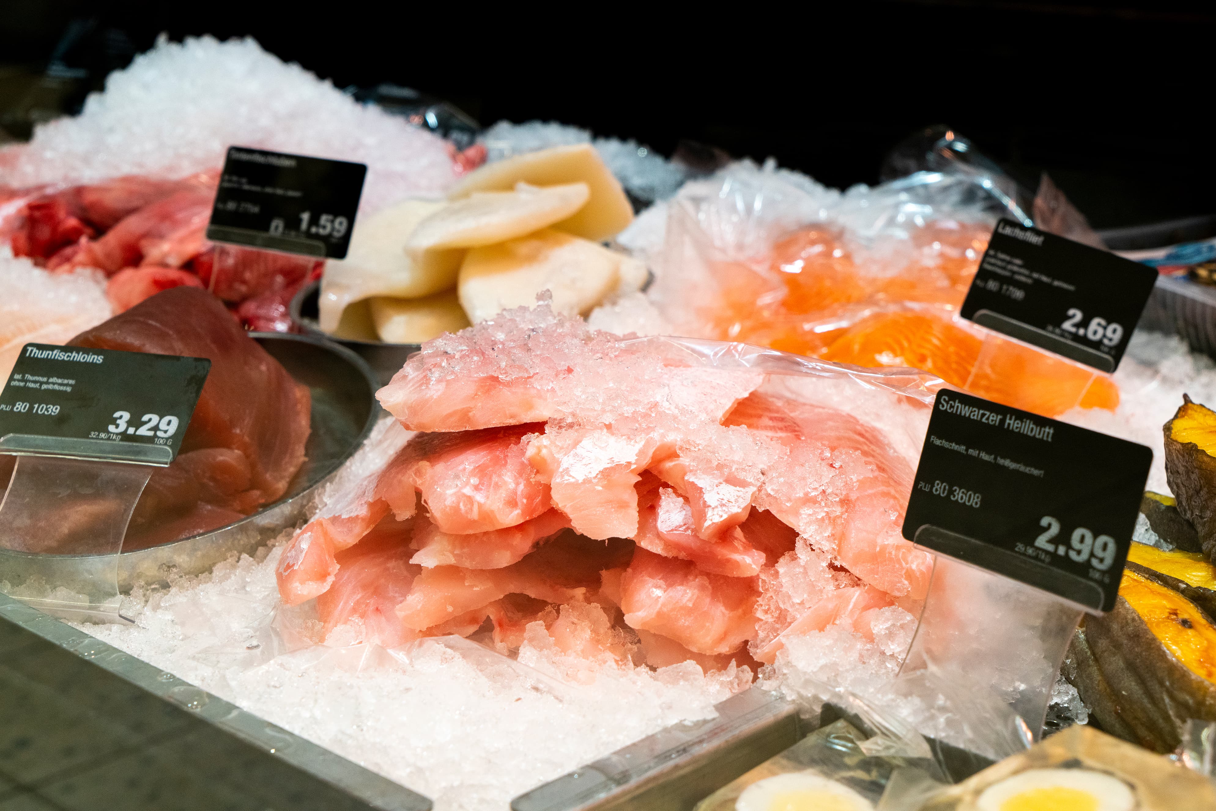Fisch in einer Auslage im Close-Up, mit Preisschildern und Obst als Deko.