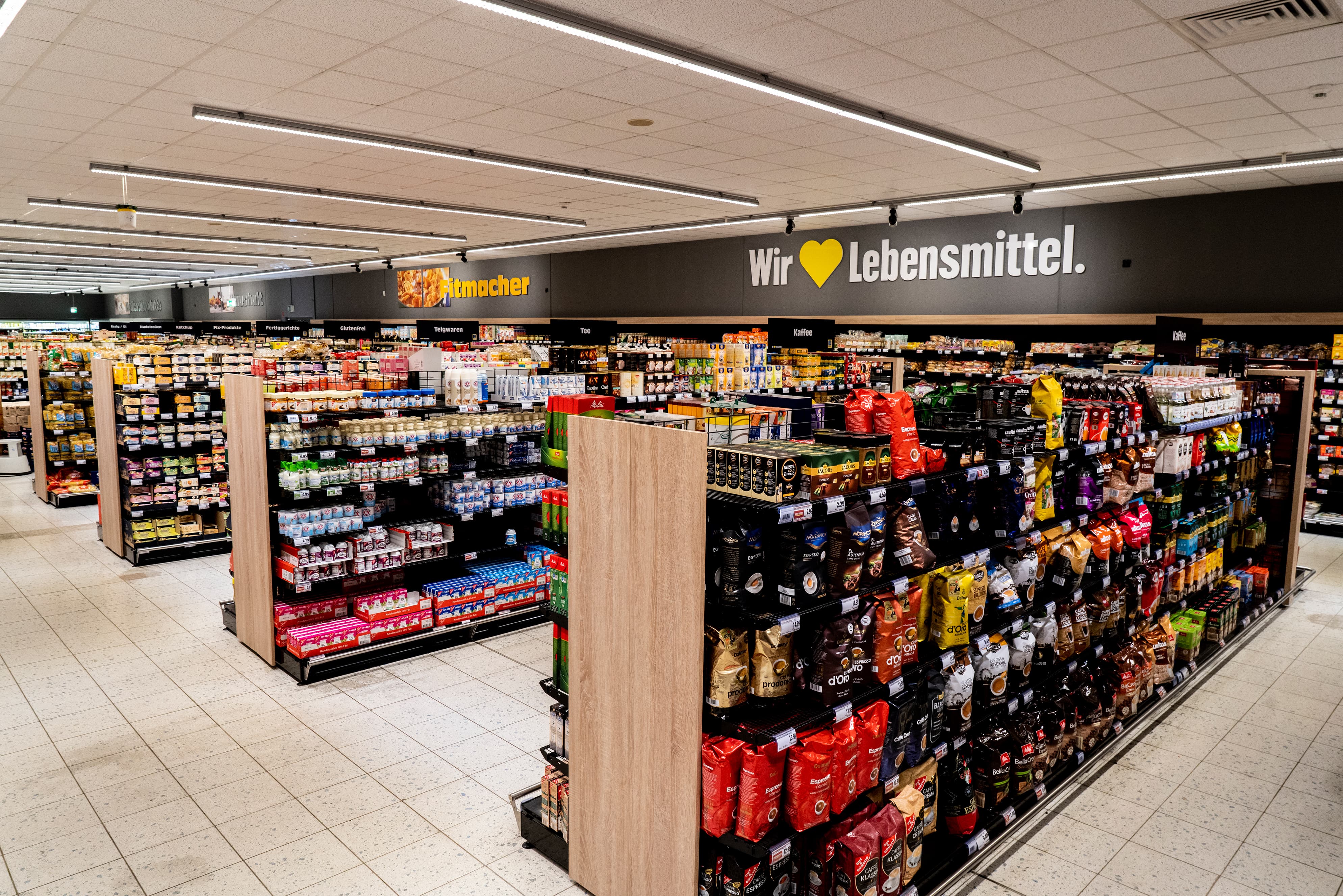 Gänge voller Produkte reihen sich in einem EDEKA-Markt auf, leicht von oben fotografiert.