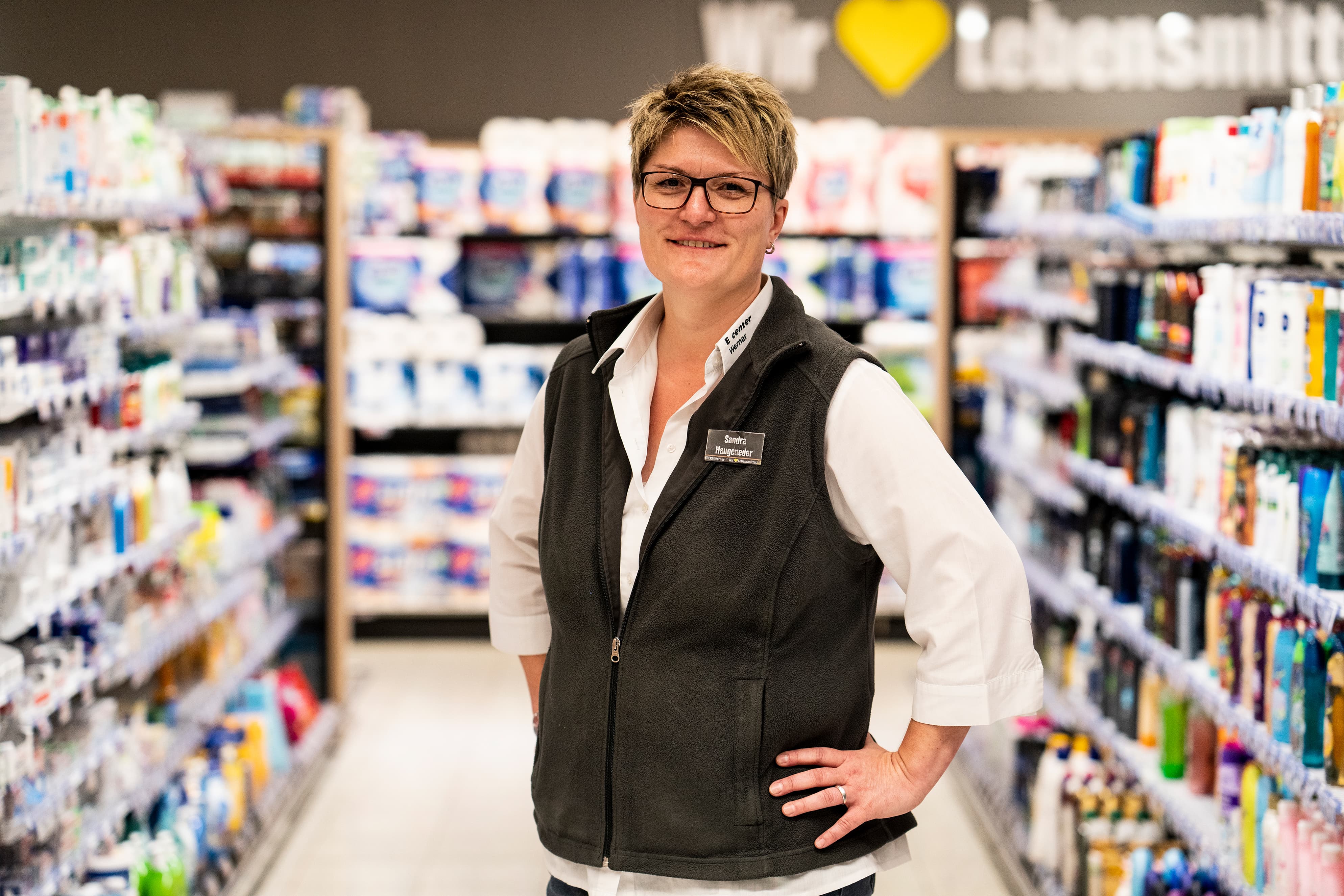 Eine Mitarbeiterin steht lächelnd im Drogeriegang eines EDEKA-Markts.