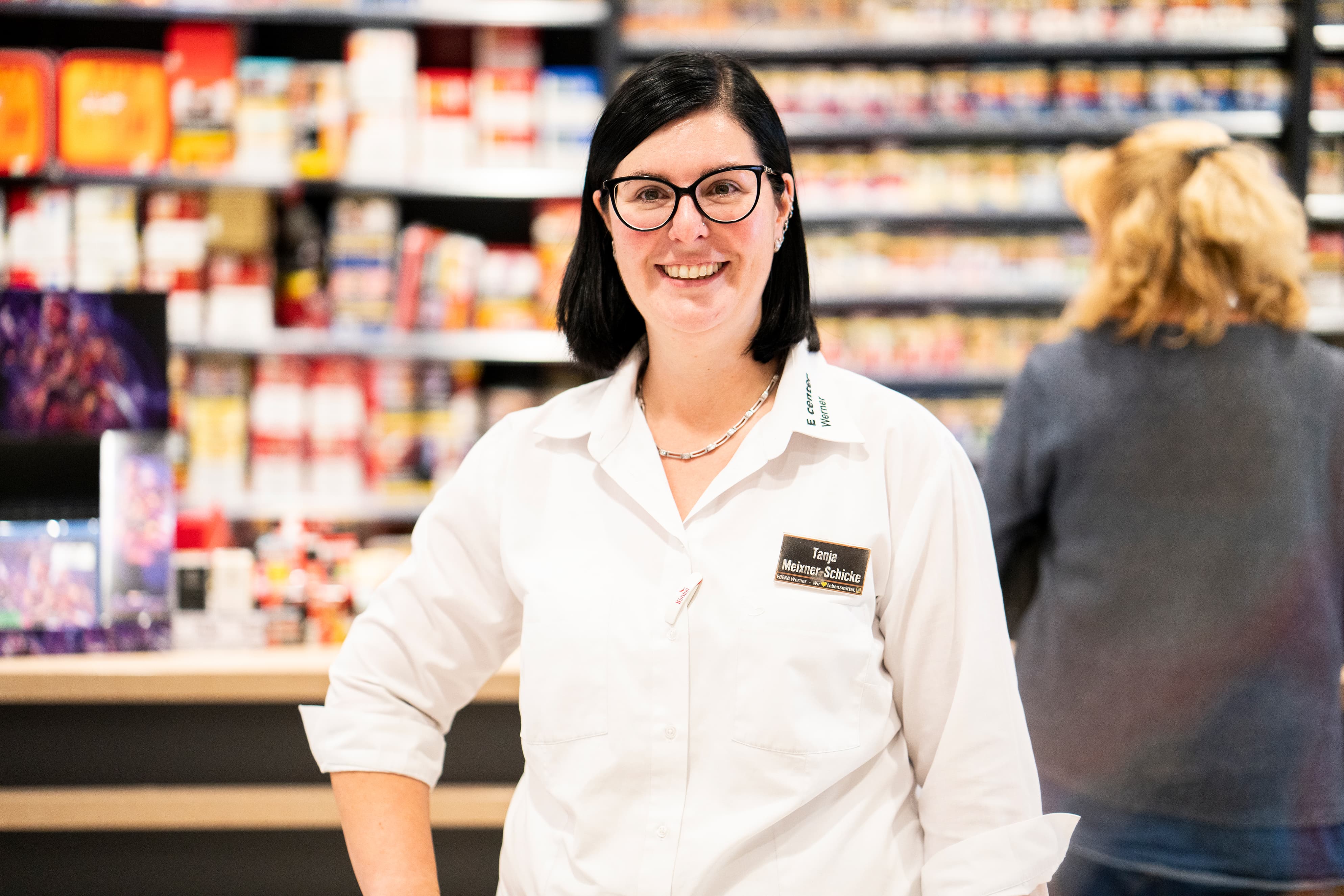 Eine Mitarbeiterin steht lächelnd vor einer Theke.