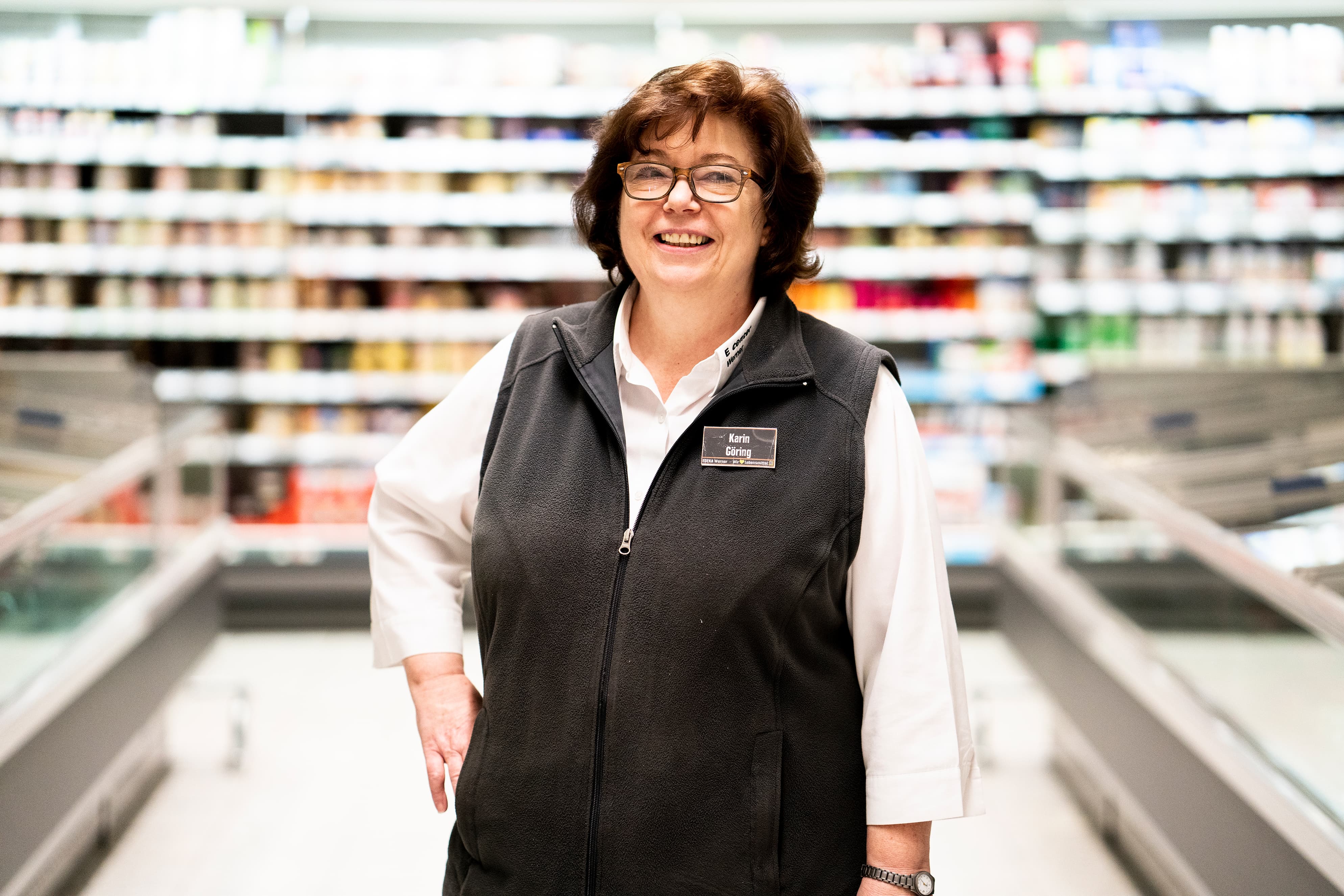 Eine Mitarbeiterin steht lächelnd im Tiefkühlbereich eines EDEKA-Markts.