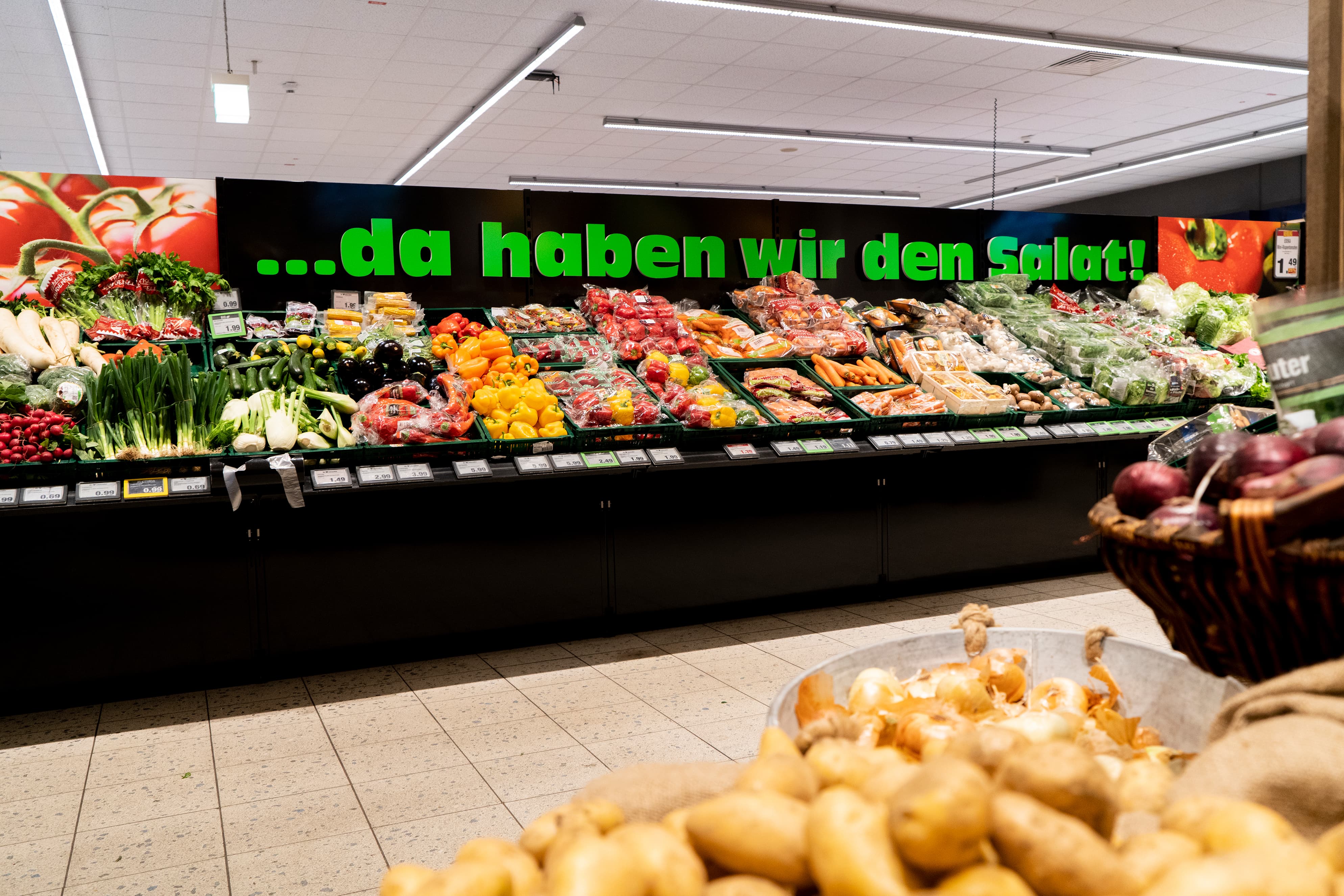 Die Gemüseabteilung eines EDEKA-Markts. Auf einem Schild steht: ... da haben wir den Salat.