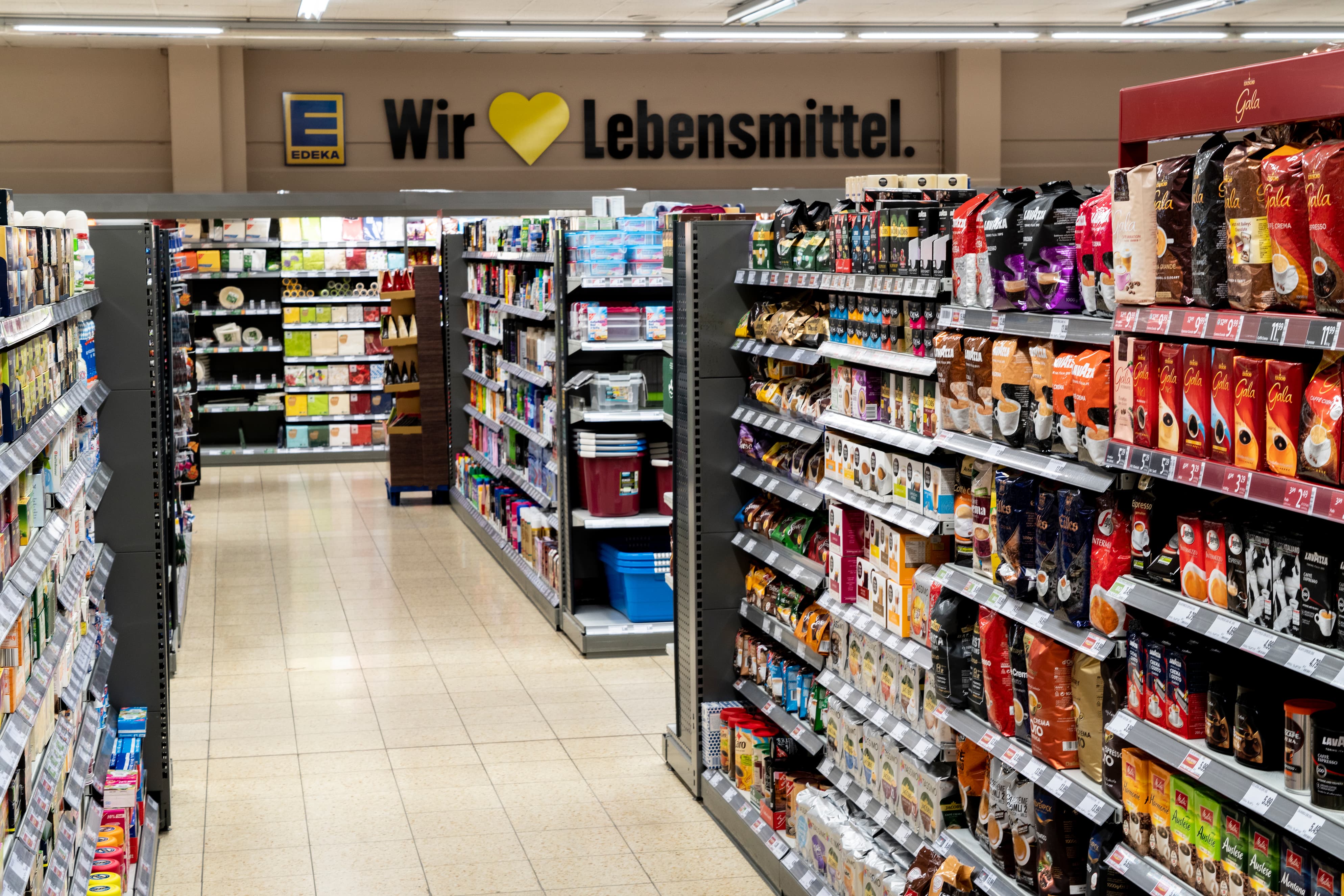 Blick in einen Gang eines EDEKA-Markts, mit verschiedenen Produkten in den Regalen. Im Hintergrund an der Wand steht: Wir lieben Lebensmittel.