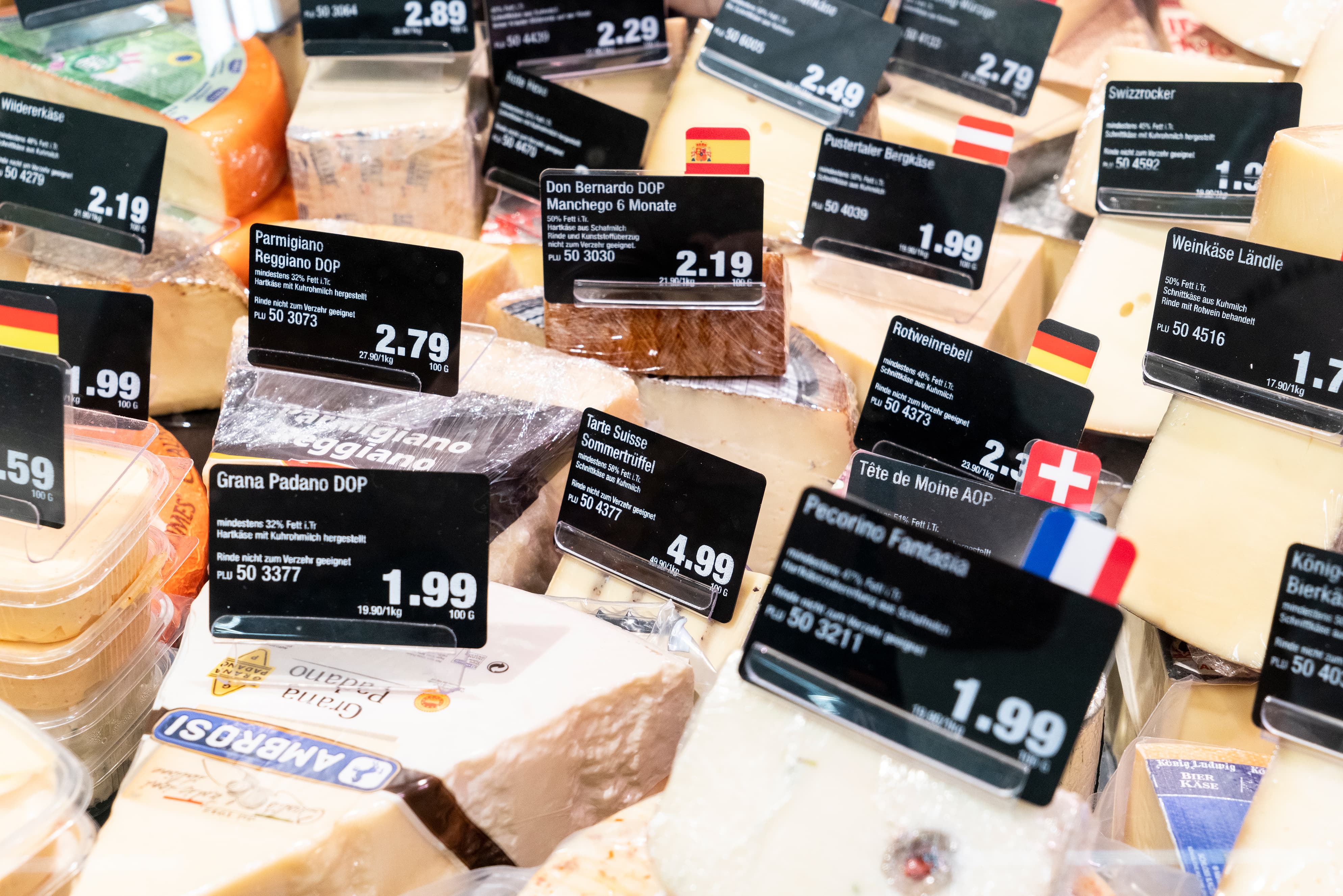 Käseauslage einer Bedienungstheke mit vielen verschiedenen Käsesorten und Preisschildern.
