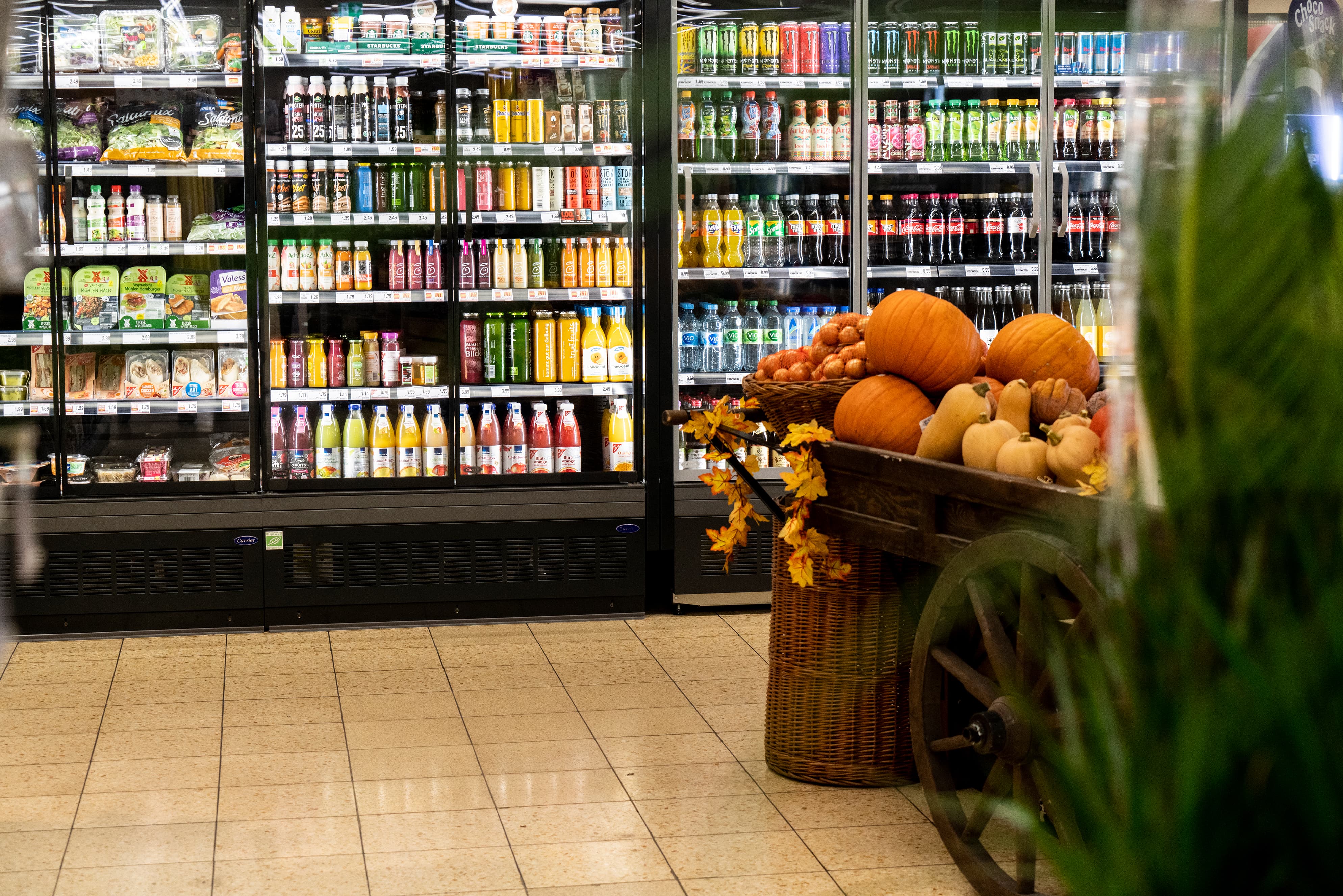 Kühlschränke mit Getränken und vegetarischen Aufschnittvarianten in einem EDEKA-Markt, im Vordergrund herbstliche Deko.