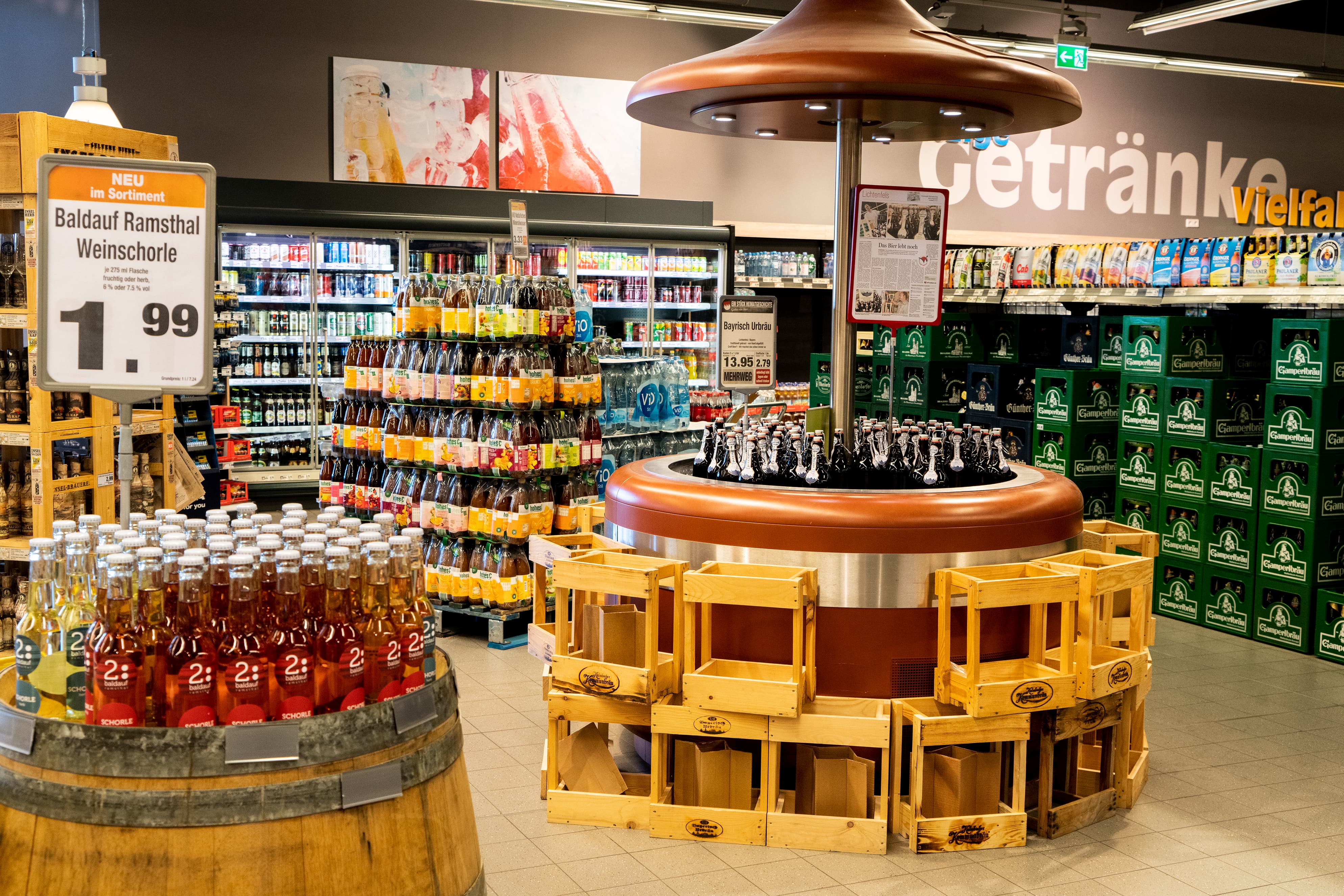 Die Getränkeabteilung eines EDEKA-Markts. Im Vodergrund steht eine Produktinsel voller Bier, die von einem riesigen Pilz überdacht wird.