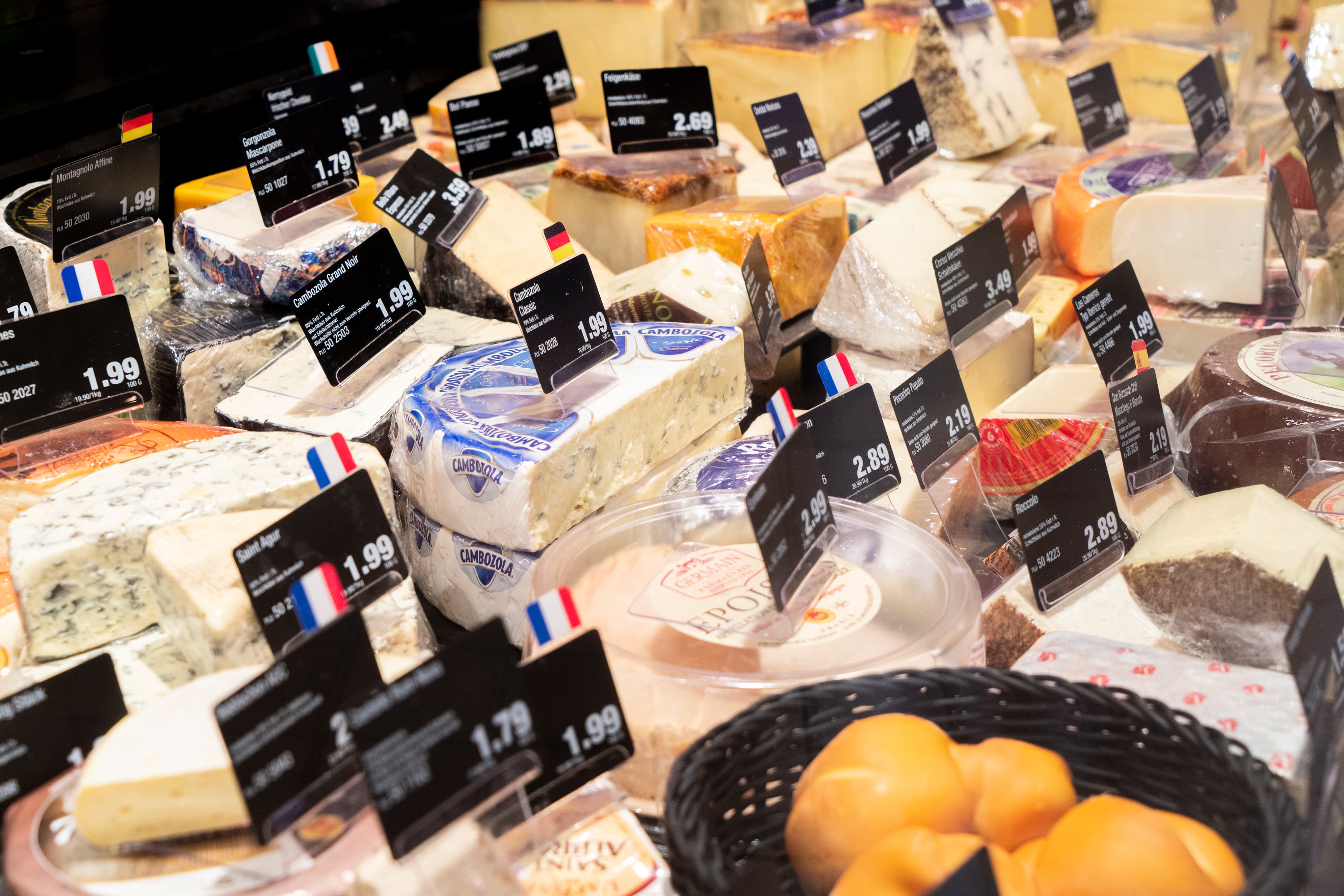 Käseauslage einer Bedienungstheke mit vielen verschiedenen Käsesorten und Preisschildern.