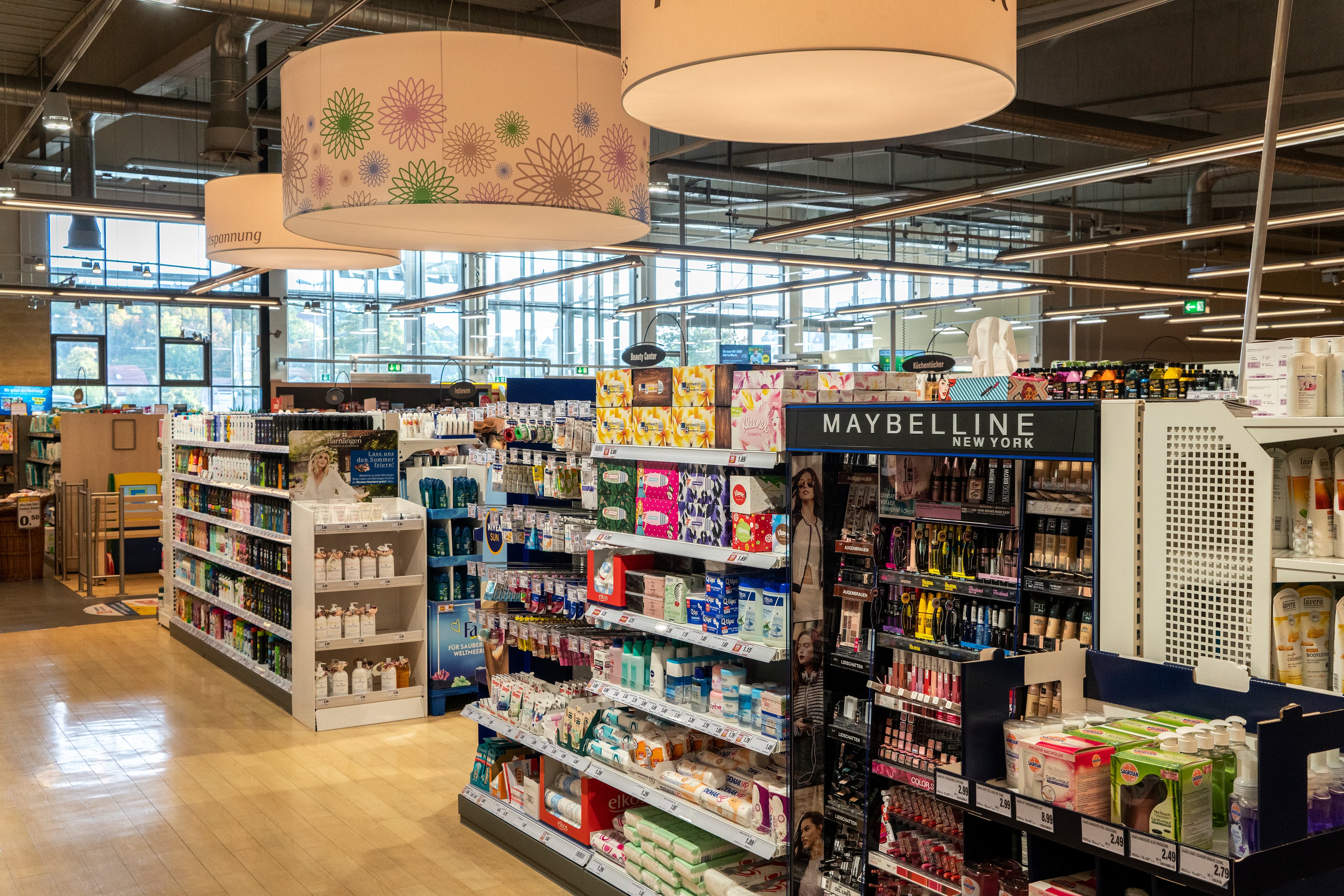 Ein moderner EDEKA-Markt von innen, mit großen Hängelampen, Fensterfronten und unzähligen Produktregalen.