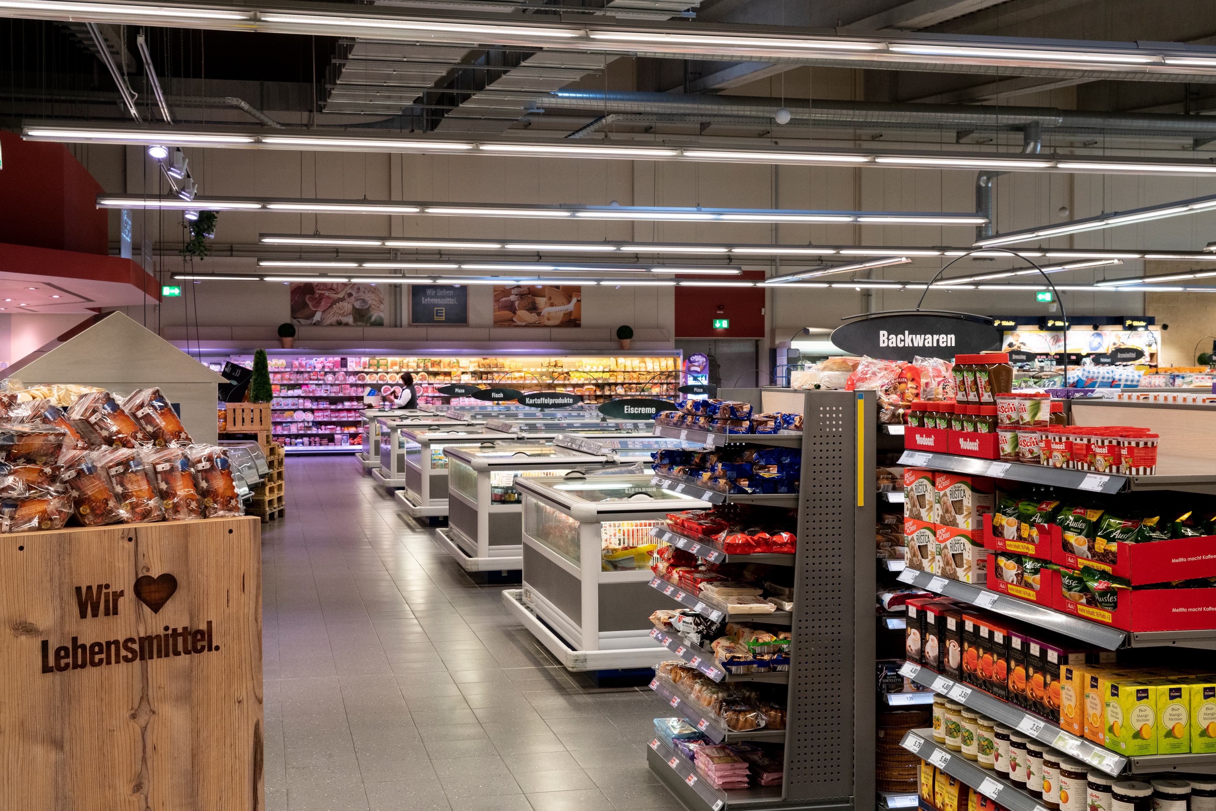 Gänge voller Produkte reihen sich in einem EDEKA-Markt auf. Im Hintergrund die Tiefkühlabteilung.