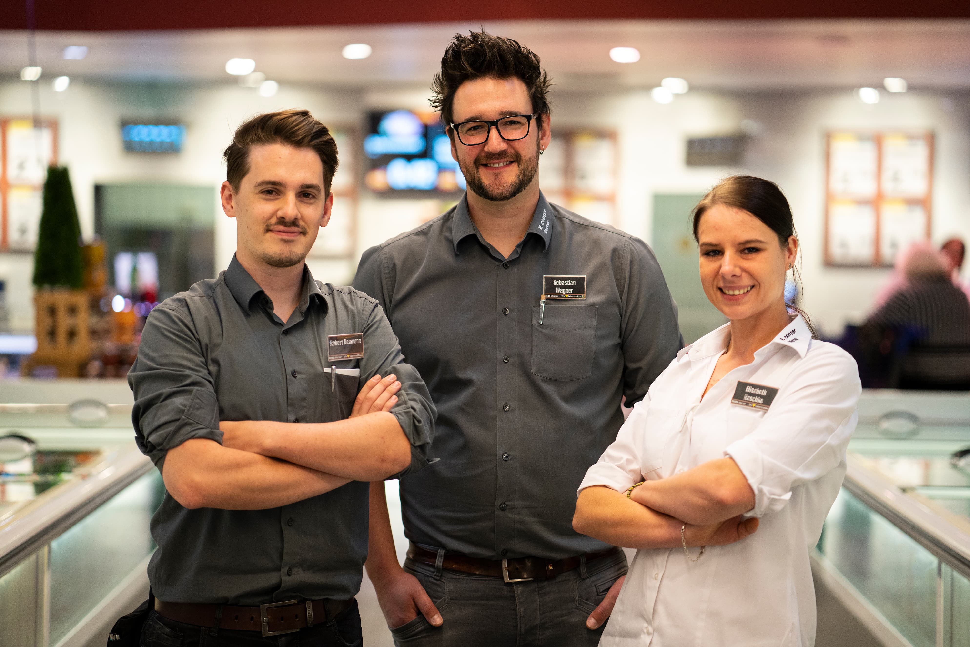 Drei junge Mitarbeitende dieses EDEKA-Markts stehen lächelnd zwischen Tiefkühltruhen.
