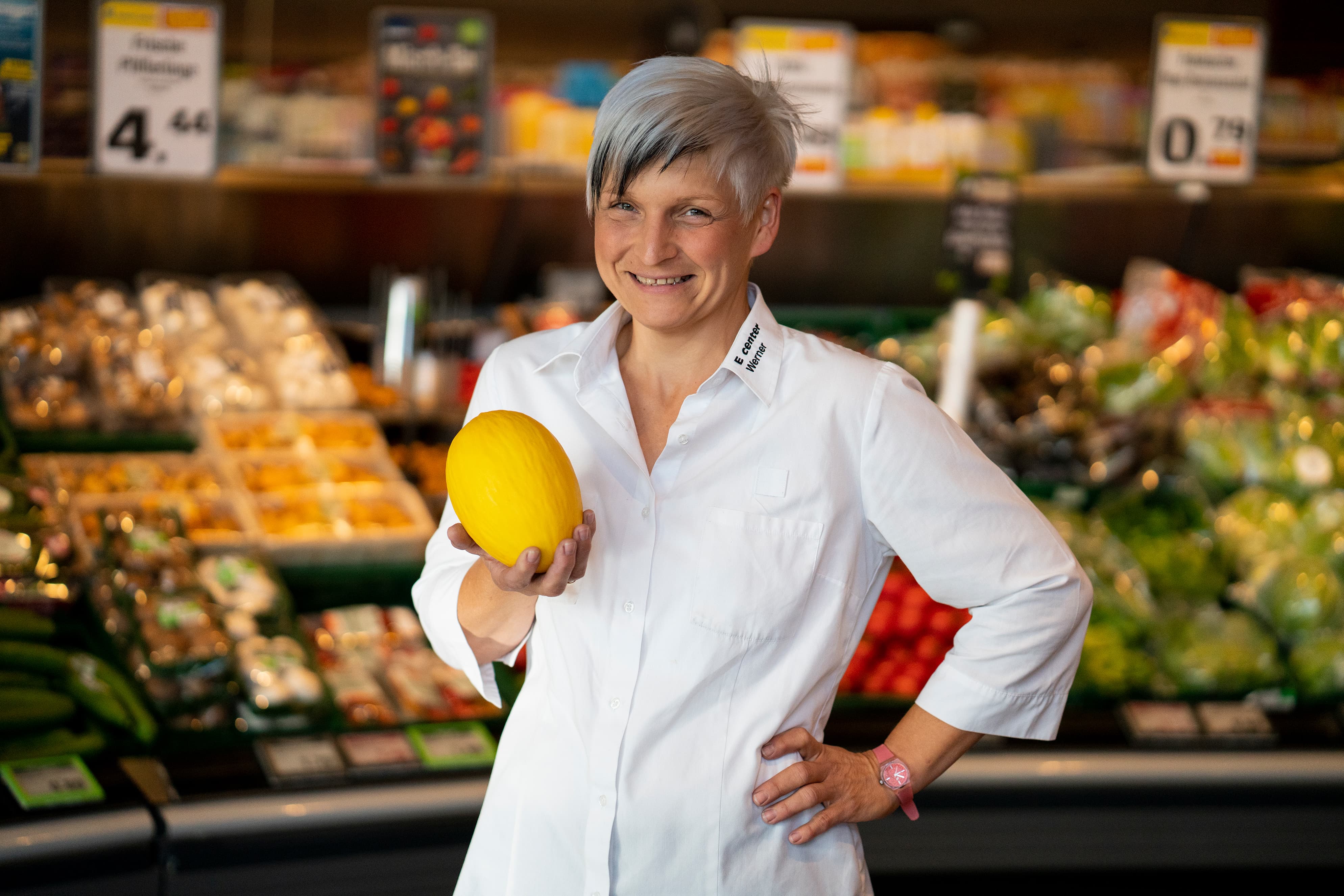 Eine Mitarbeiterin steht lächelnd in der Obst- und Gemüseabteilung eines EDEKA-Markts.