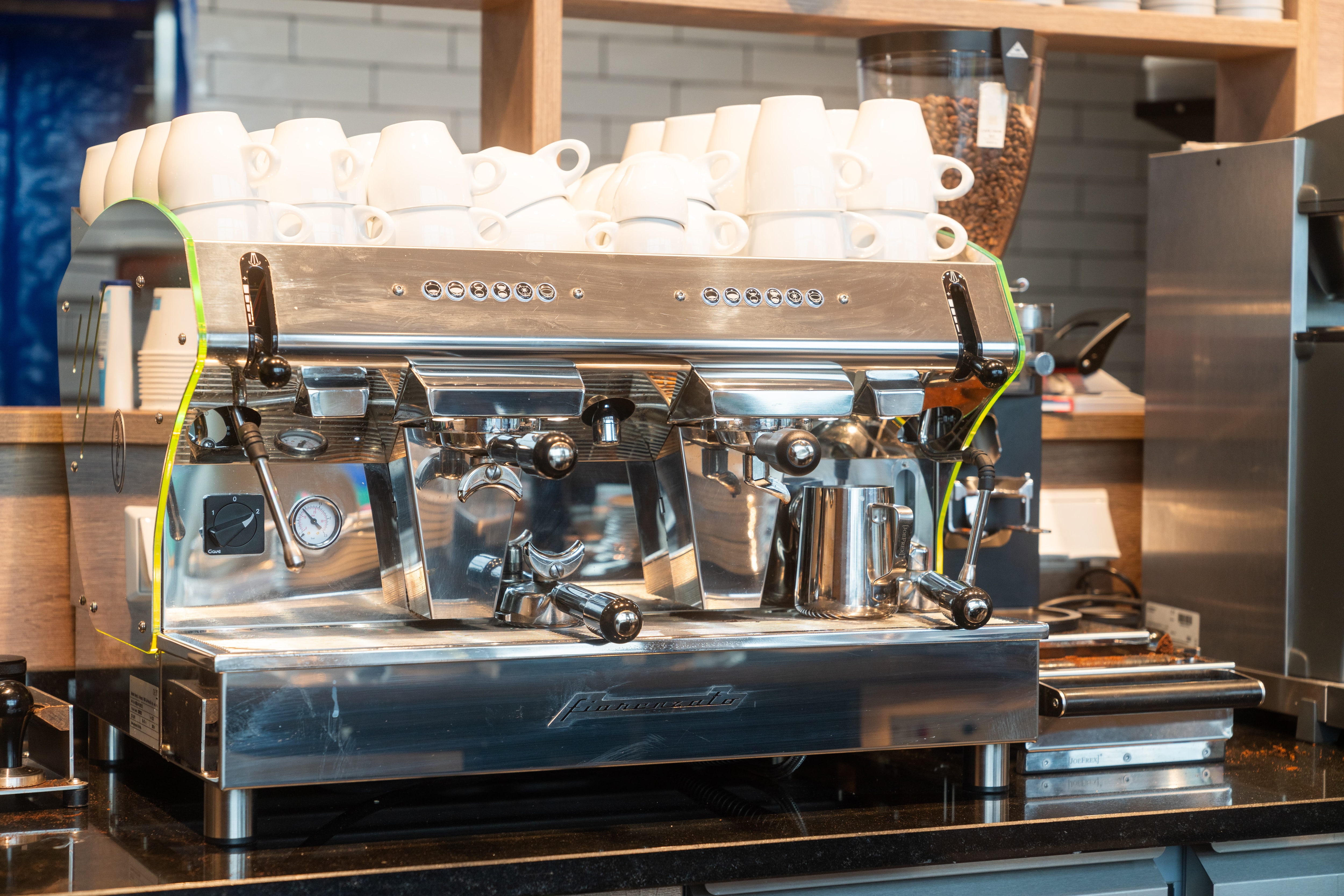 Eine silberne Siebträger Kaffeemaschine mit weißen Tassen auf der Deckel-Ablage.