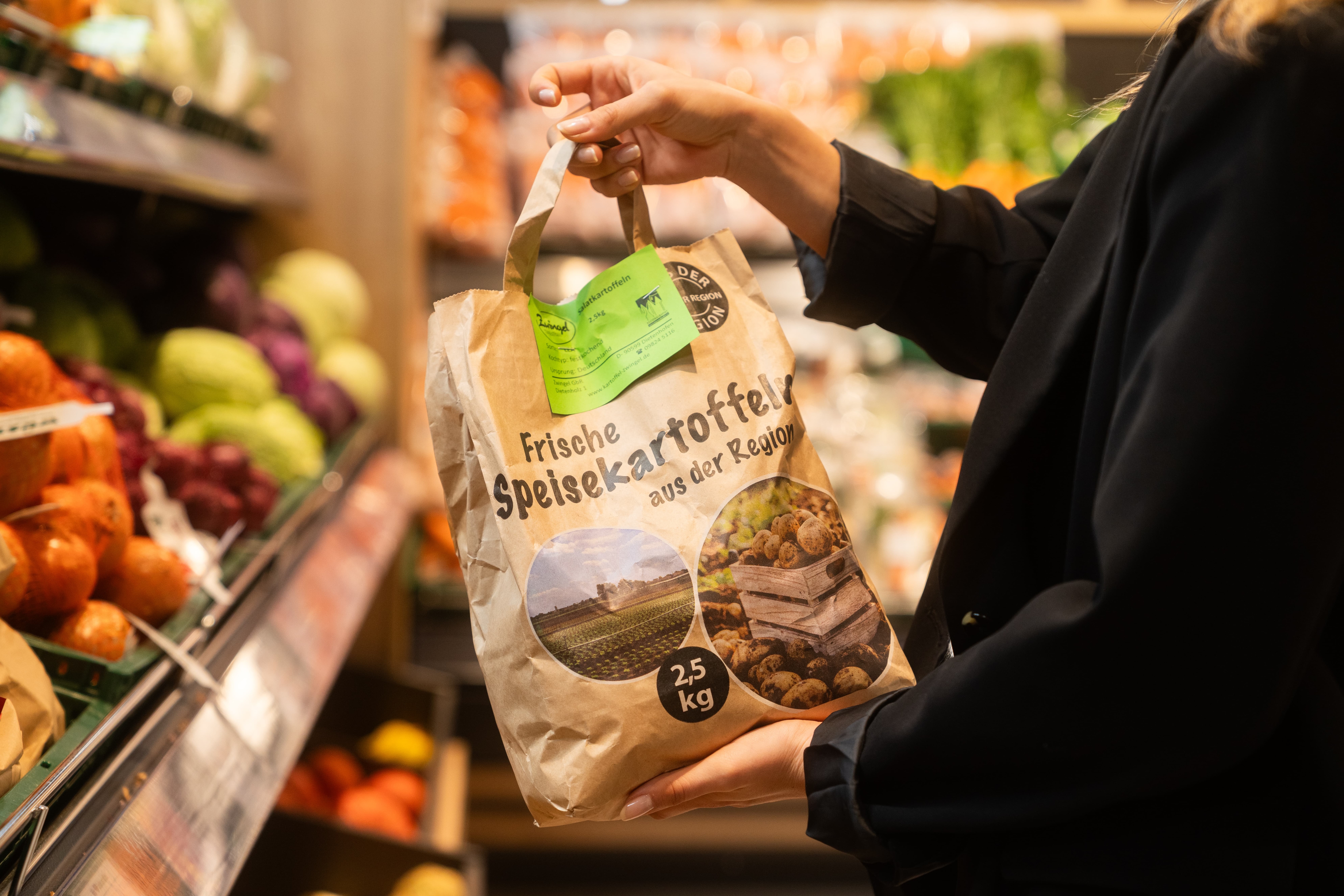 Eine Frau hält eine 2,5 kg Papierpackung Kartoffeln hoch.