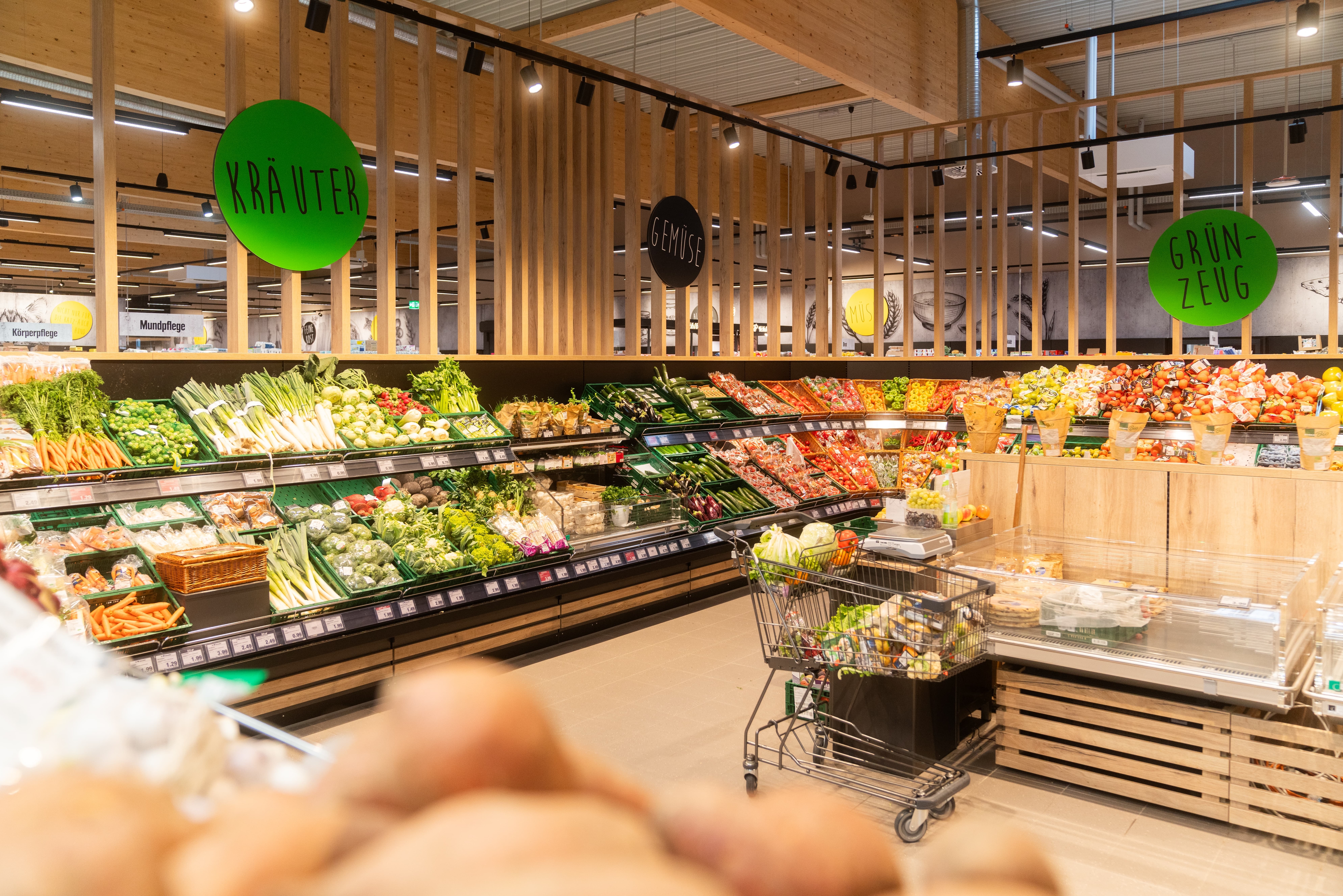 Gemüseabteilung aus der Totalen. Über den Regalen stehen die Wörter Kräuter, Gemüse und Grünzeug.