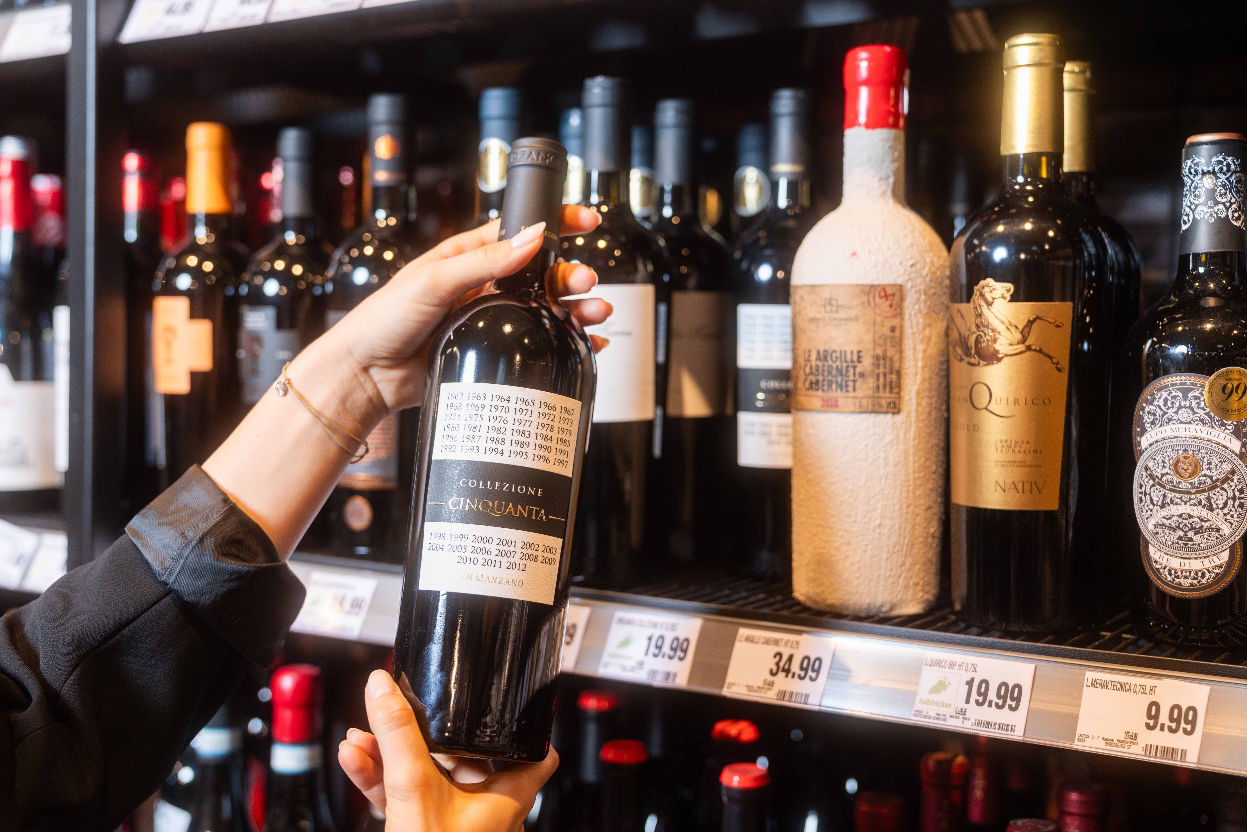 Person hält Rotweinflasche in der Hand, die sie aus dem Regal nimmt.