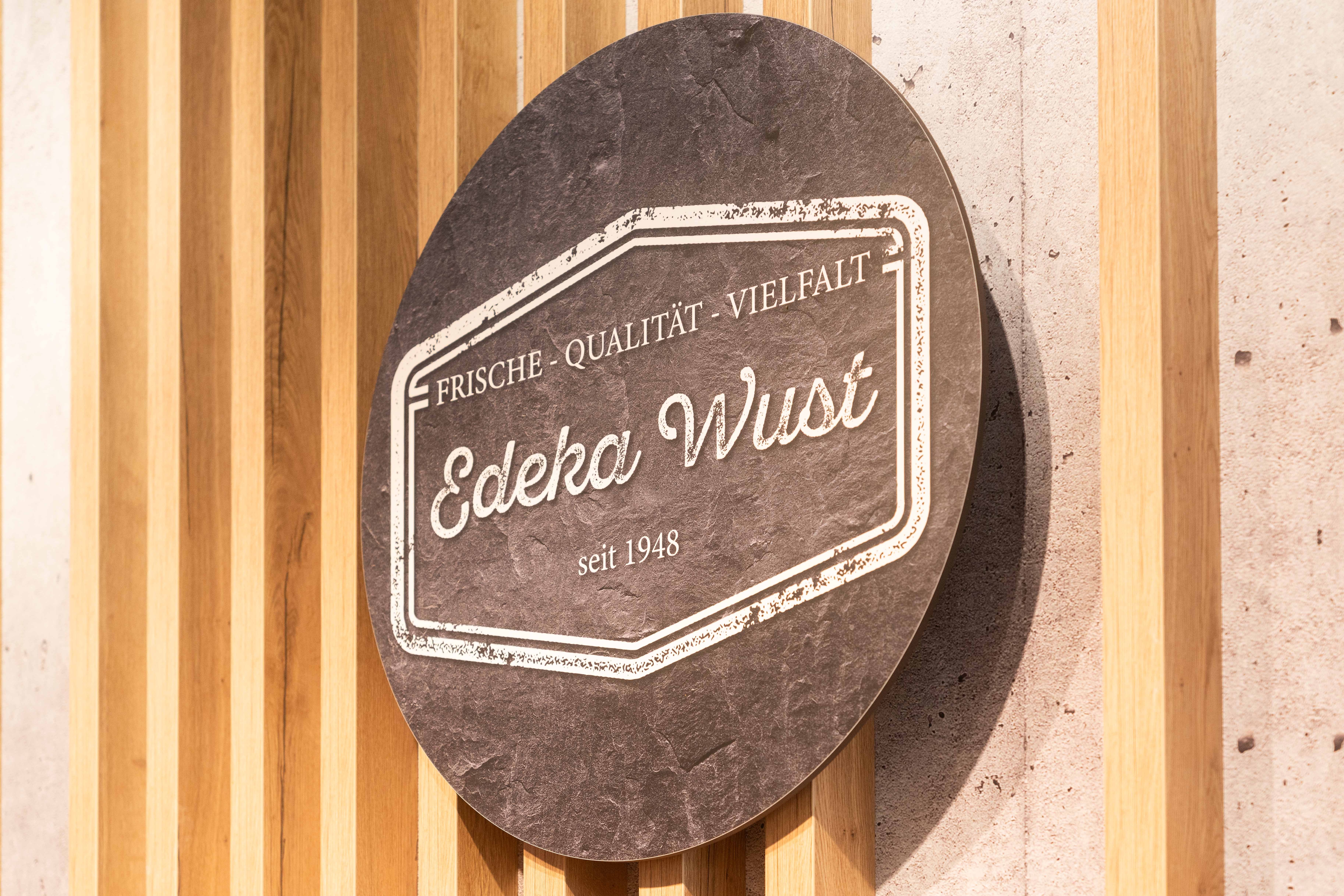An der Wand hängt ein rundes Schild mit dem Logo von EDEKA Wust.