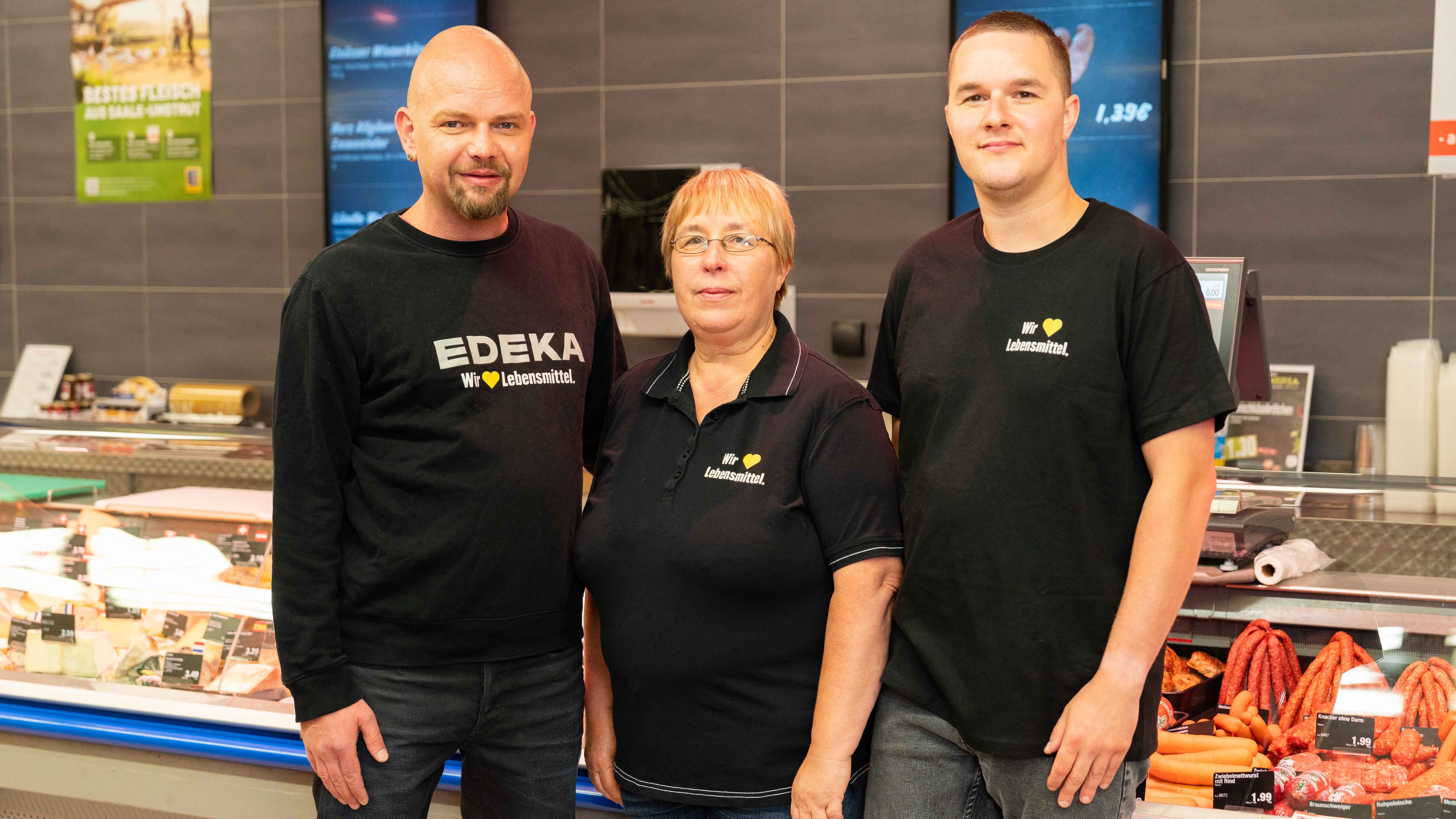 Vor der Frischetheke stehen 3 Mitarbeitende in EDEKA T-Shirts, eine Frau und zwei Männer.