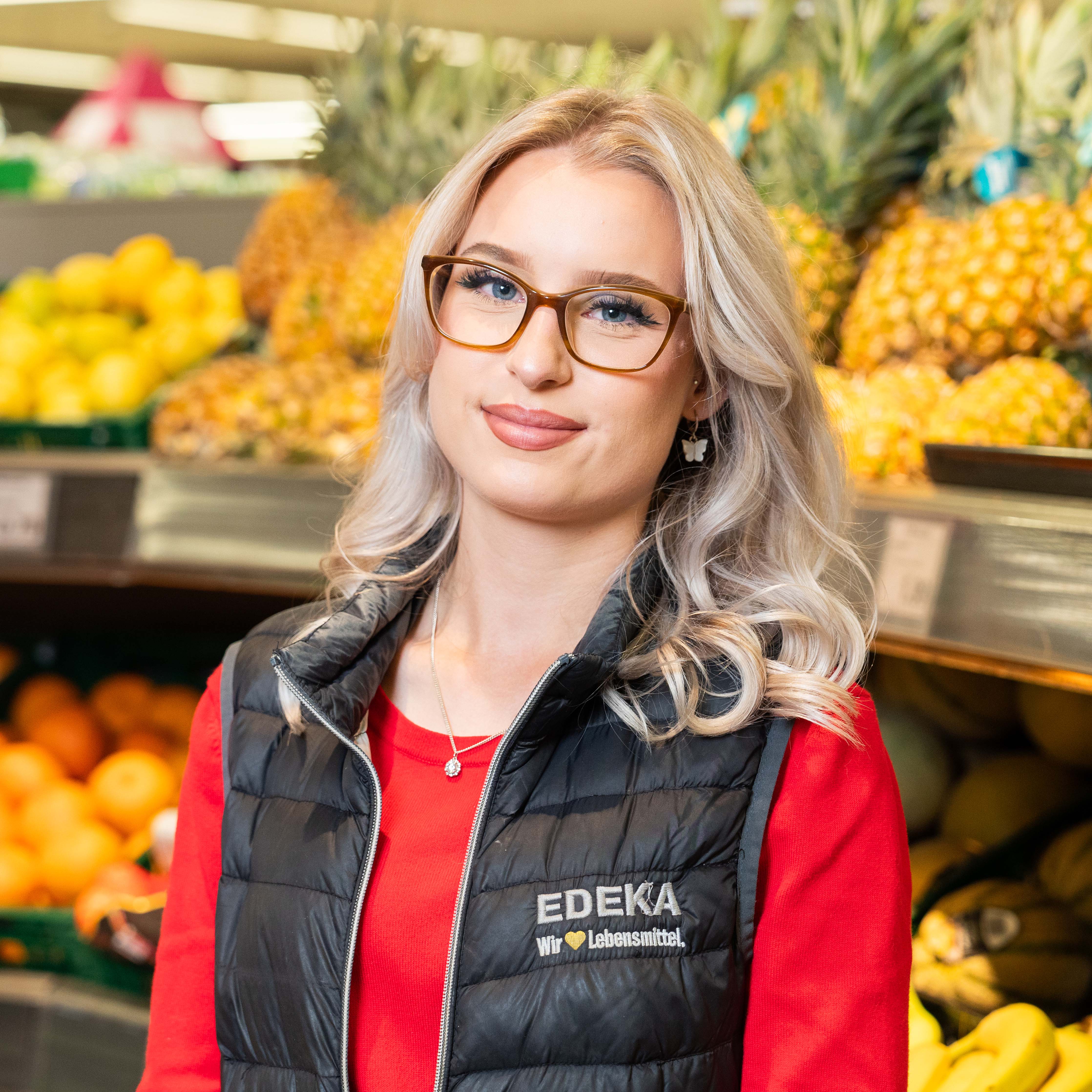 Eine Azubine mit EDEKA Weste steht vor dem Ananas Regal.