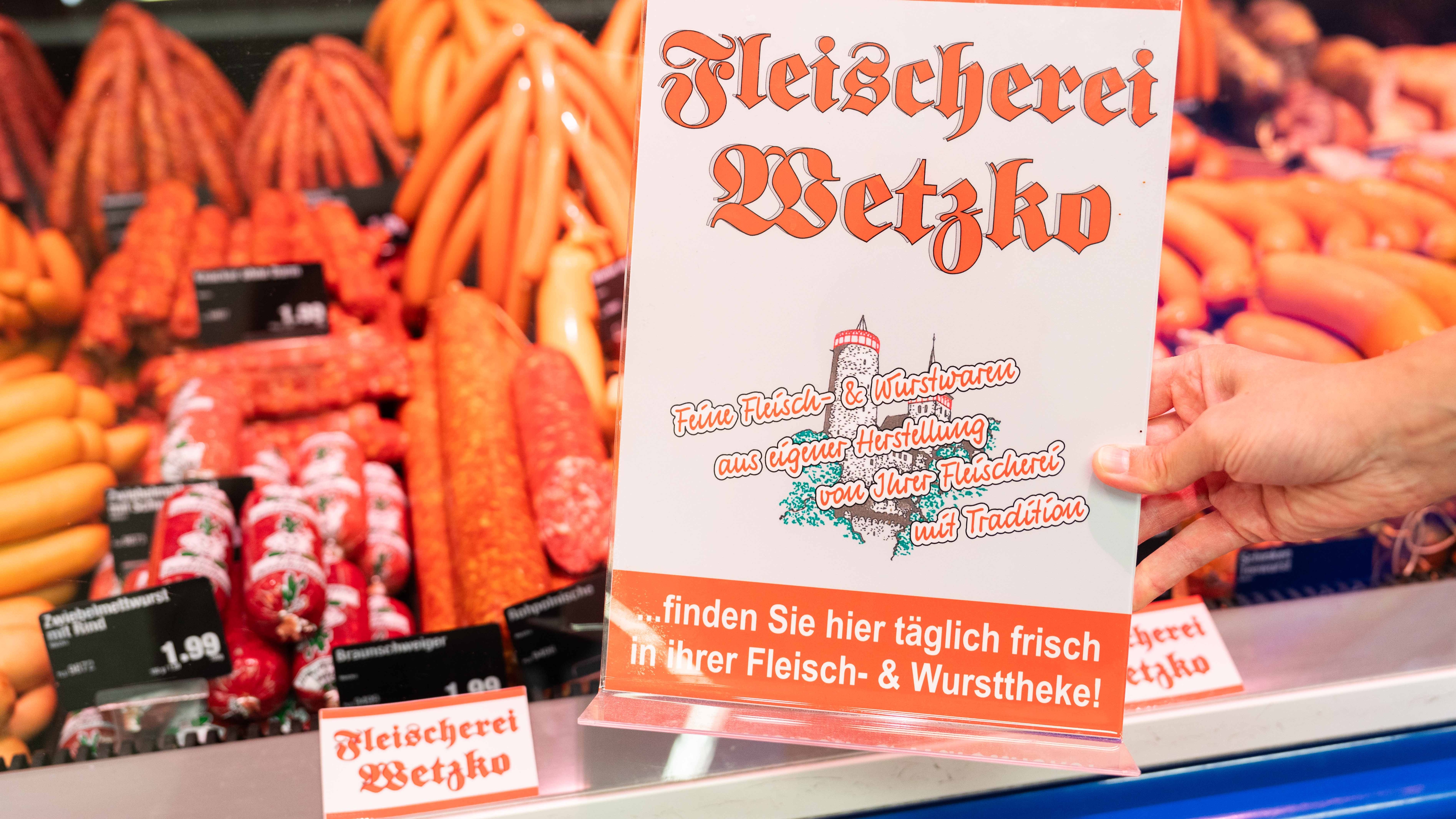 Vor die Auslage mit den Würstchen wird ein Schild der ansässigen Metzgerei Wetzko gehalten.