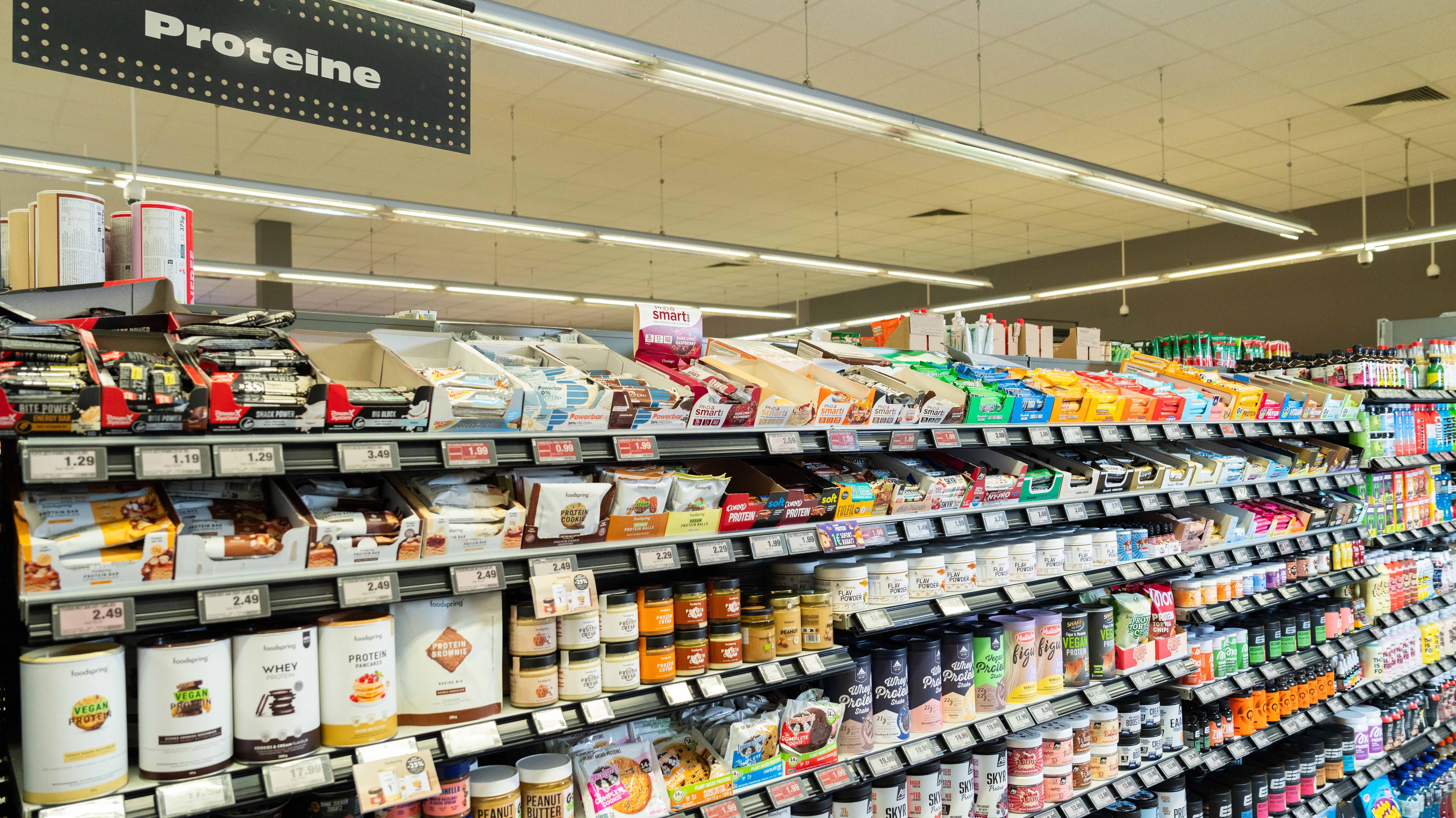 Regal mit verschiedene Proteinprodukten, wie Pulver und Riegel.