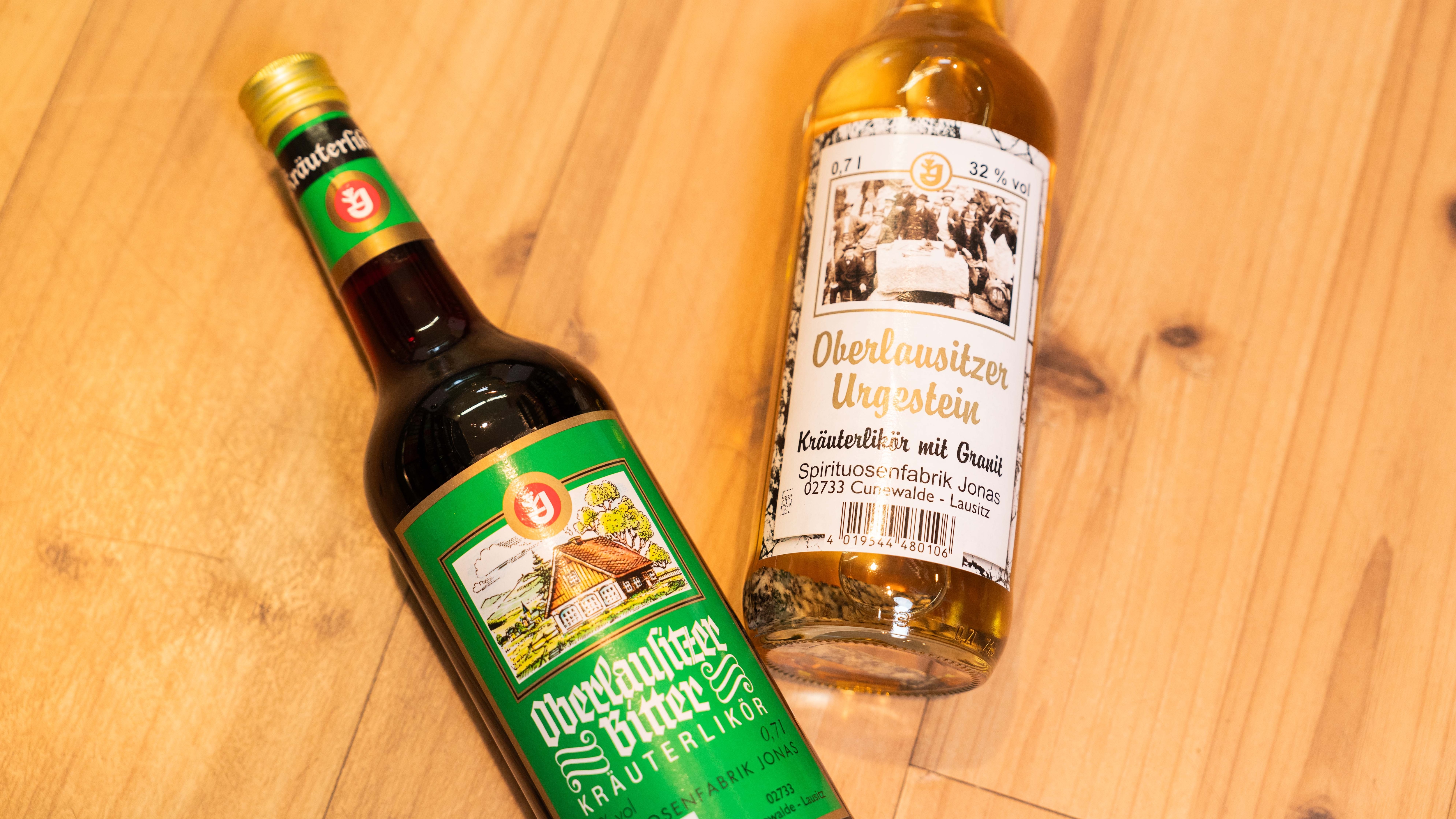 Zwei Flaschen Oberlausitzer Kräuterlikör in verschiedenen Sorten liegen dekorativ auf Holz.