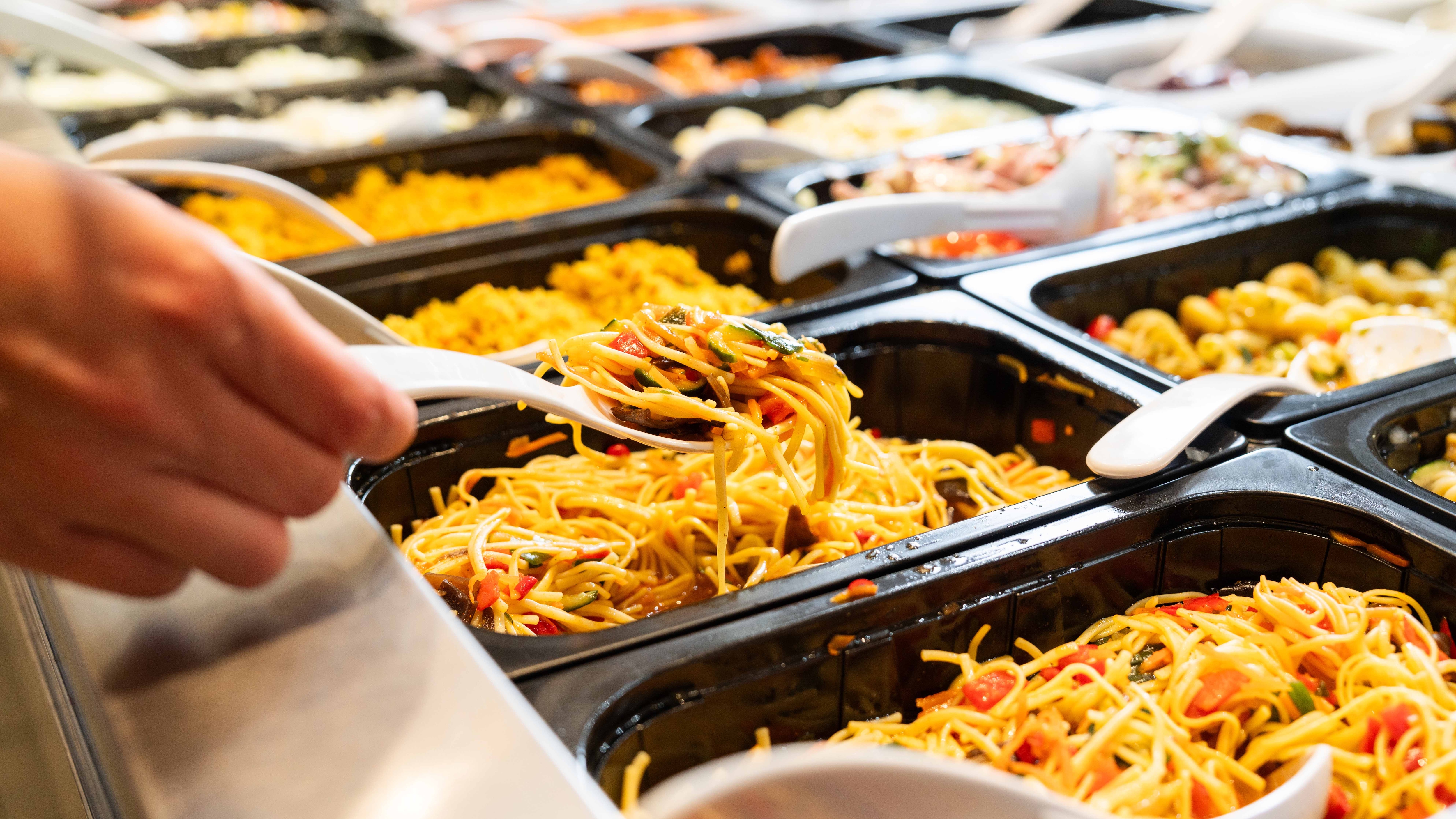Fokus auf Löffel mit Spaghettisalat, der von einer Hand herausgenommen wird bei der Salatbar.