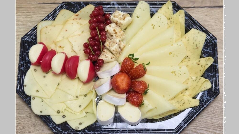 Eine Käseplatte mit verschiedenen Käsesorten, Erdbeeren und Johannisbeeren.