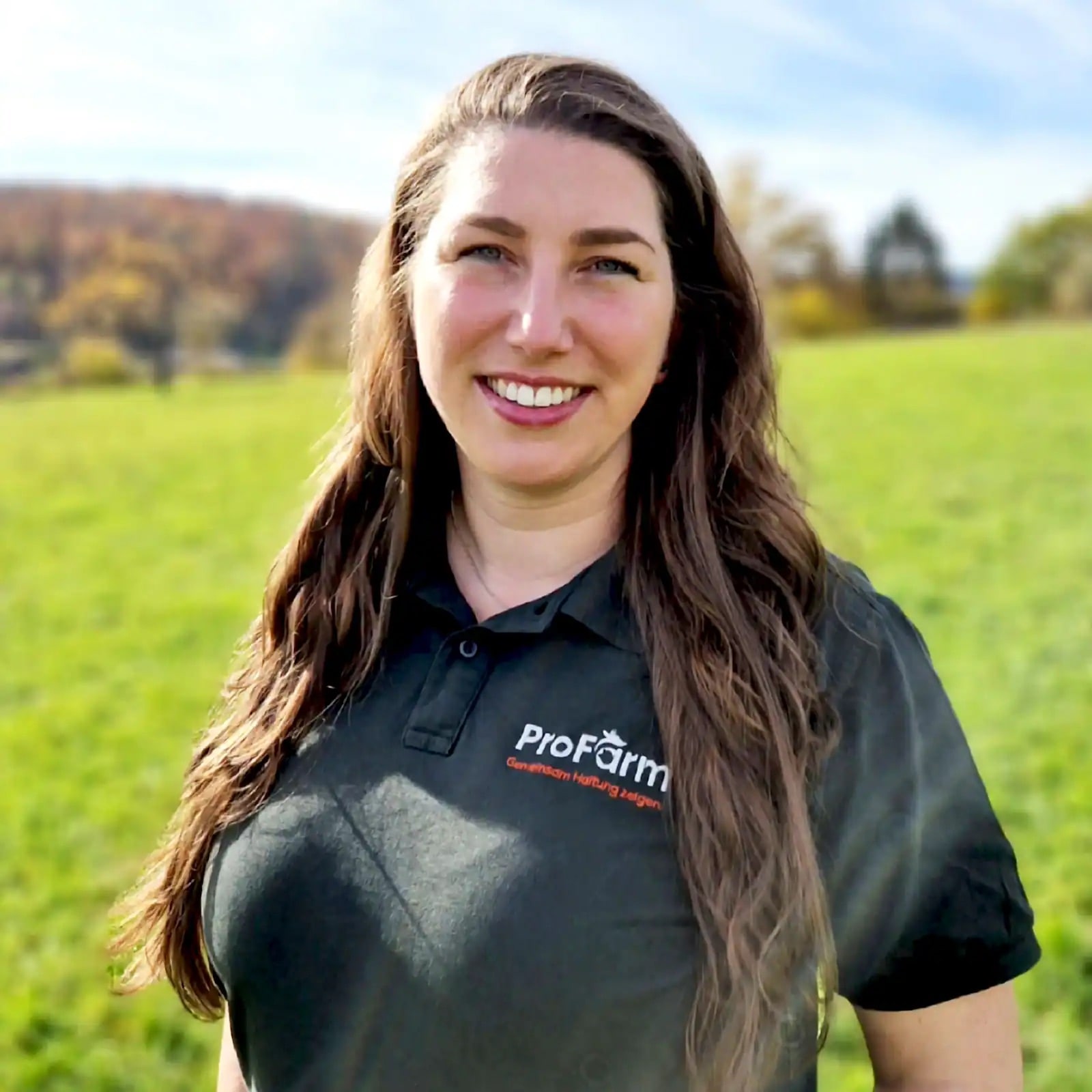 Frau steht vor einem Feld. Sie trägt ein dunkelgrünes Poloshirt mit Logo von ProFarm.