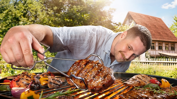 Ein Mann hält mit einer Grillzange ein Steak über einem Grill in der Hand.