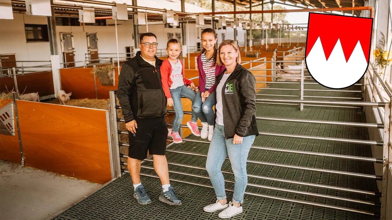 Ein Mann und eine Frau sowie zwei Kleinkinder in einem Schweinestall. Oben rechts ein Wappen mit drei weißen Zacken auf rotem Hintergrund.