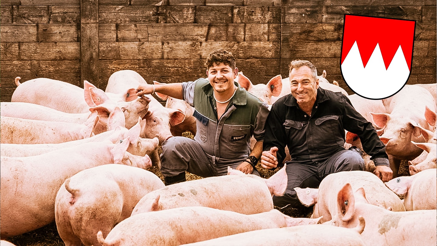 Zwei Bauern knien lächelnd zwischen einigen Hausschweinen.