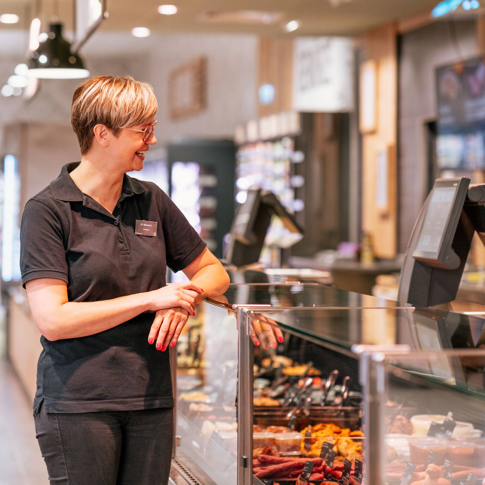 Eine Frau in schwarzem Poloshirt steht an die Fleischtheke eines Supermarktes gelehnt.
