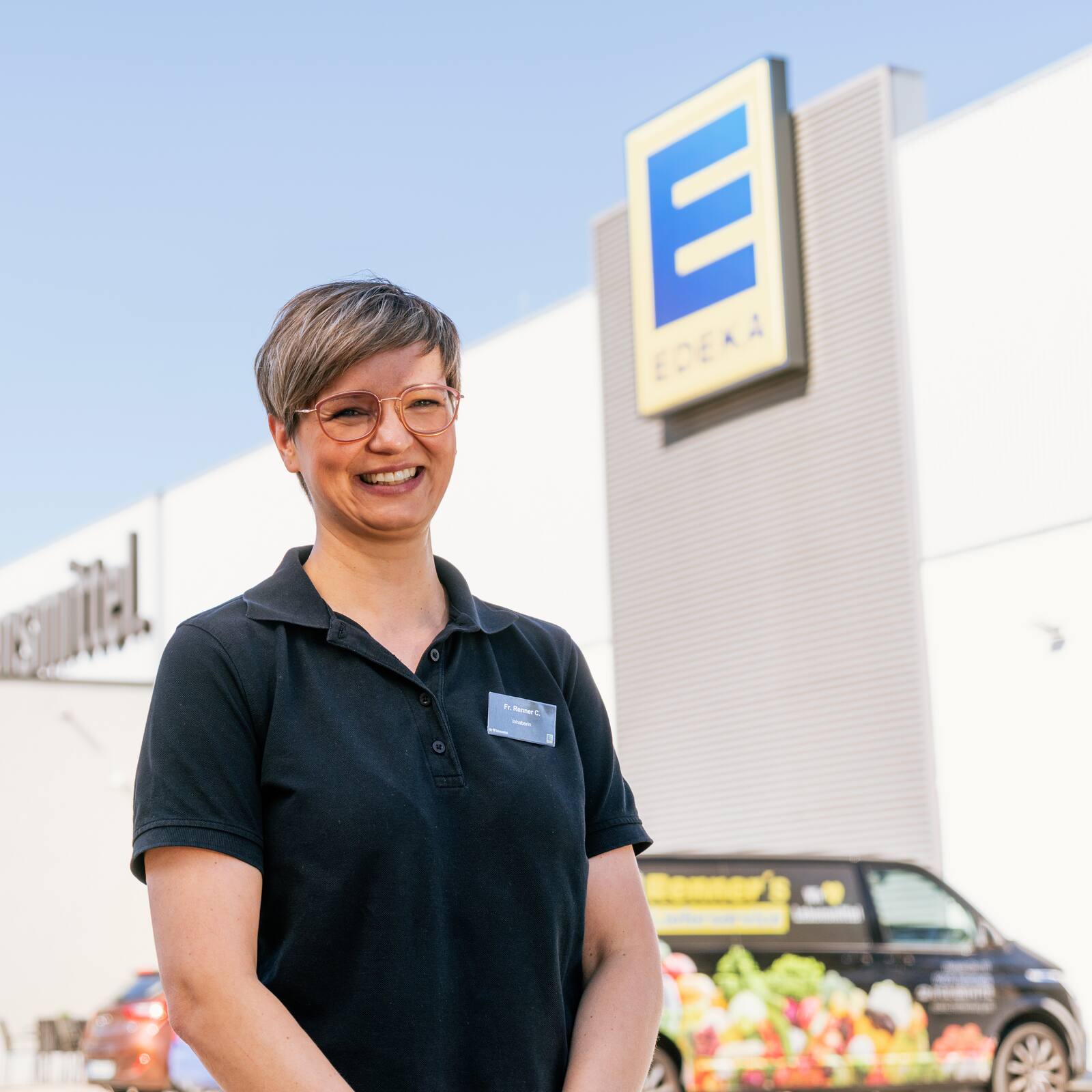 Die Inhaberin Chris Renner steht lachend vor dem Eingang ihres Supermarktes.