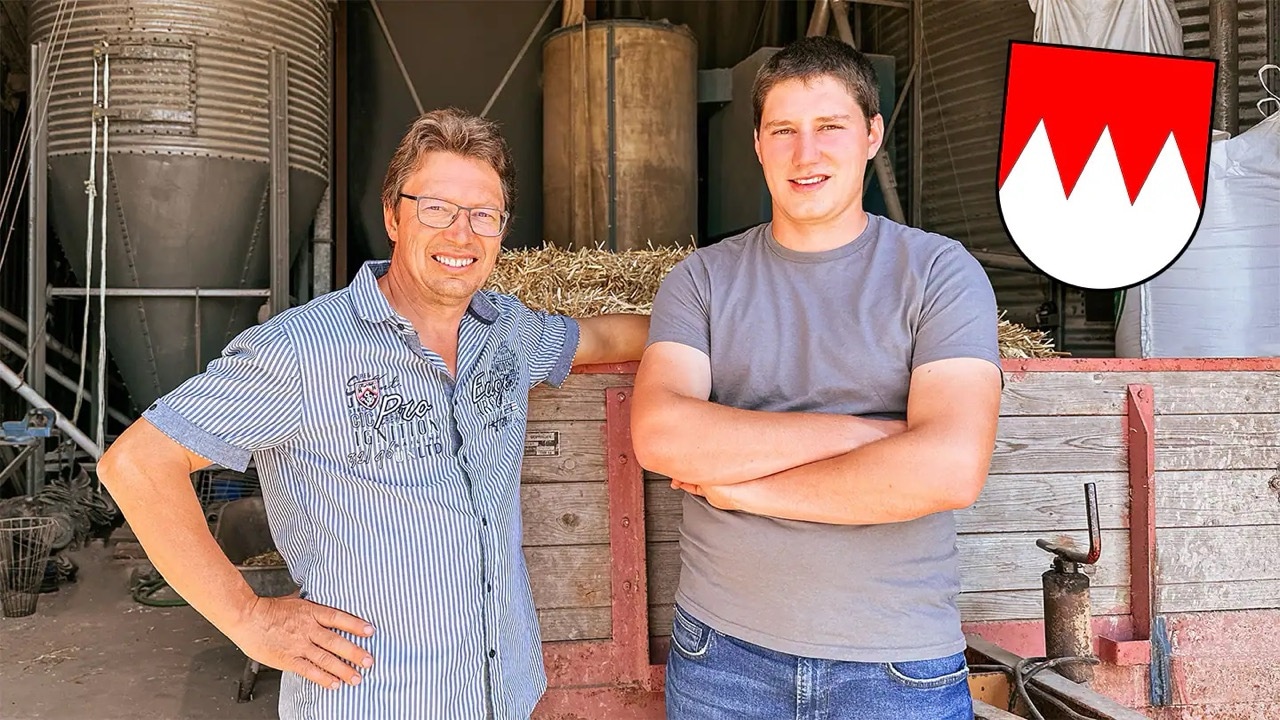Ein junger und ein älterer Mann stehen vor einem Anhänger mit Heu.