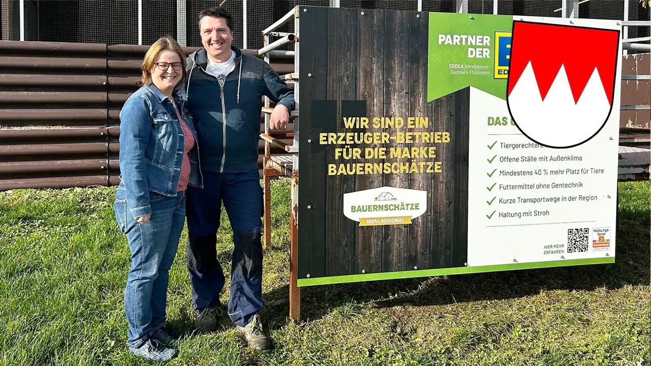 Ein Mann und eine Frau stehen vor einem großen Schild: Wir sind ein Erzeuger-Betrieb für die Marke Bauernschätze.