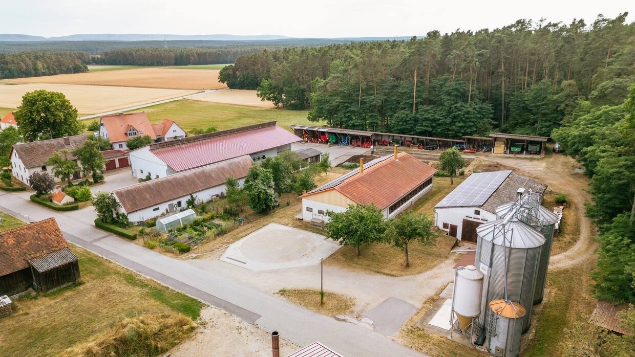 Luftaufnahme des Hofes von Familie Kübler. Im Hintergrund Felder und ein Waldstück.