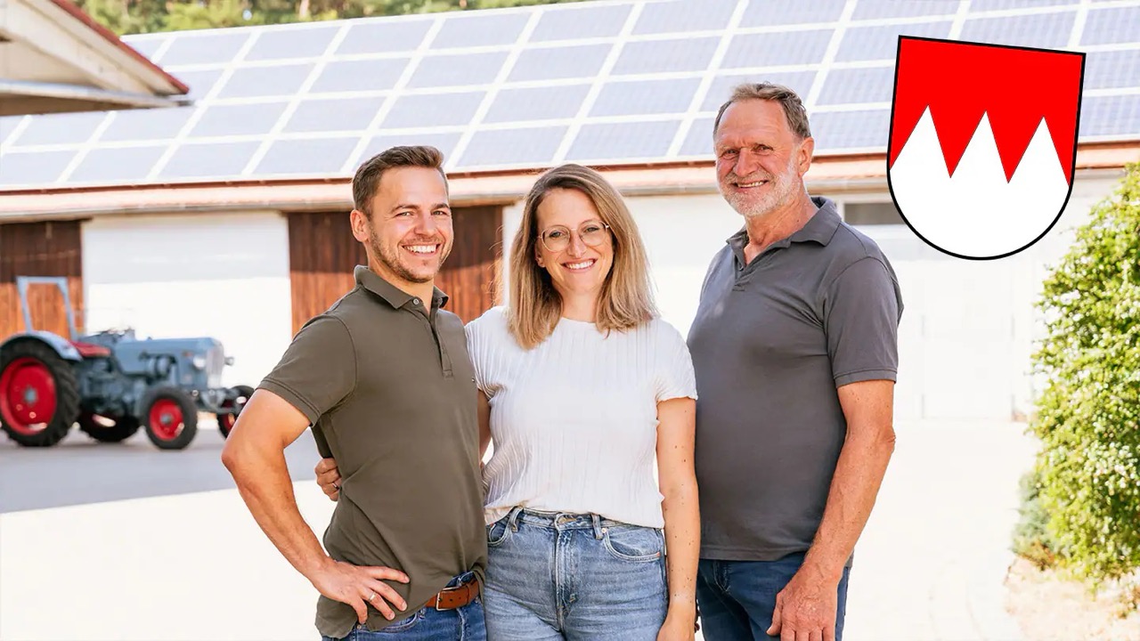 Drei Personen vor einer Halle, dessen Dach mit Solarzellen ausgestattet ist.