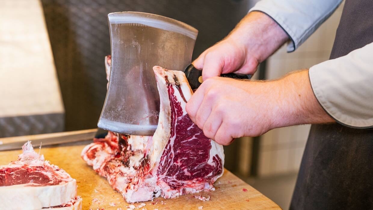 Ein Mann mit Metzgerschürze zerlegt ein Stück Fleisch mit einem Beil.