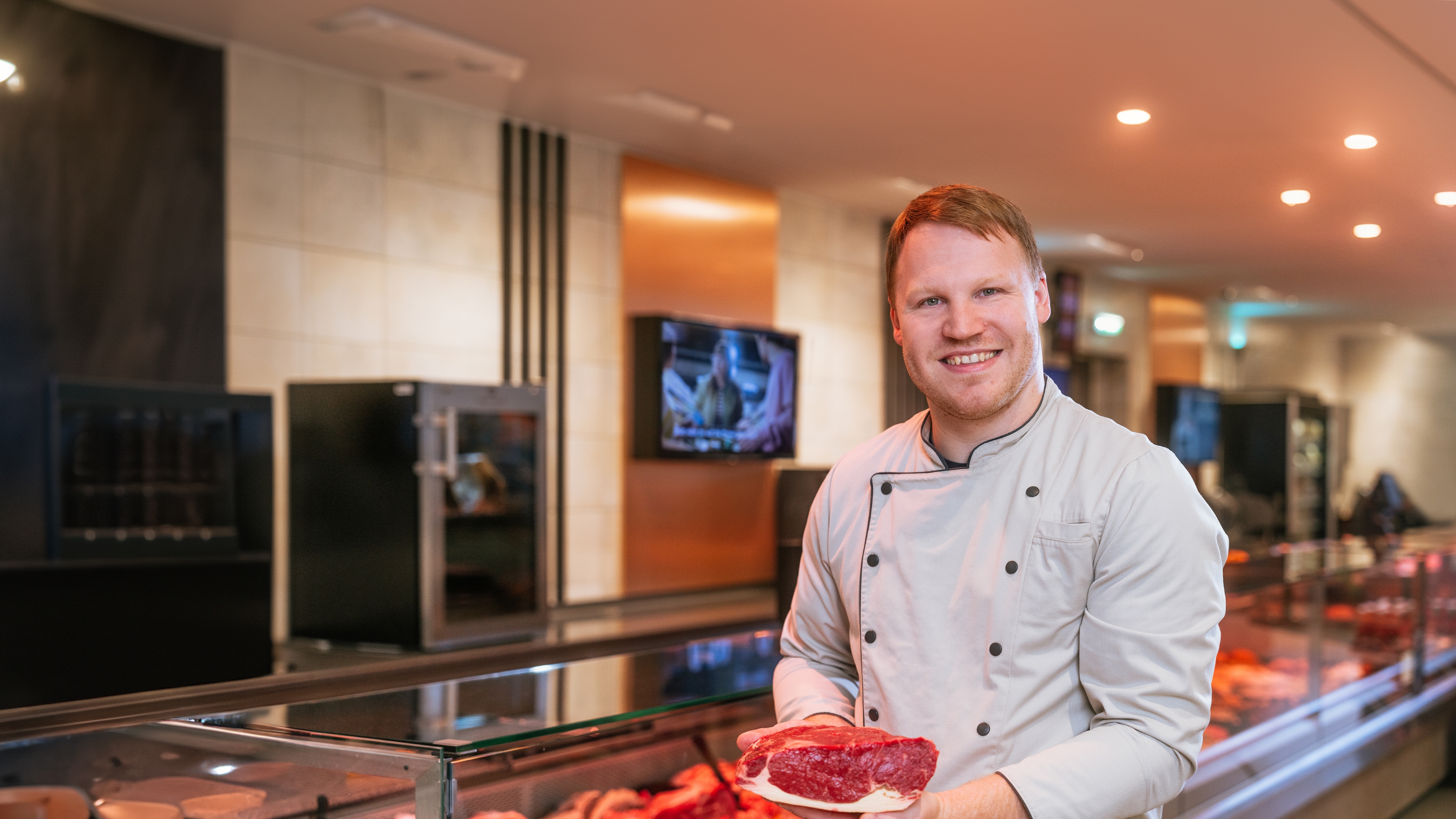 Marius Schliermann vom Edeka Schliermann hält ein Stück Fleisch in der Hand und steht lächelnd vor der Frischetheke.