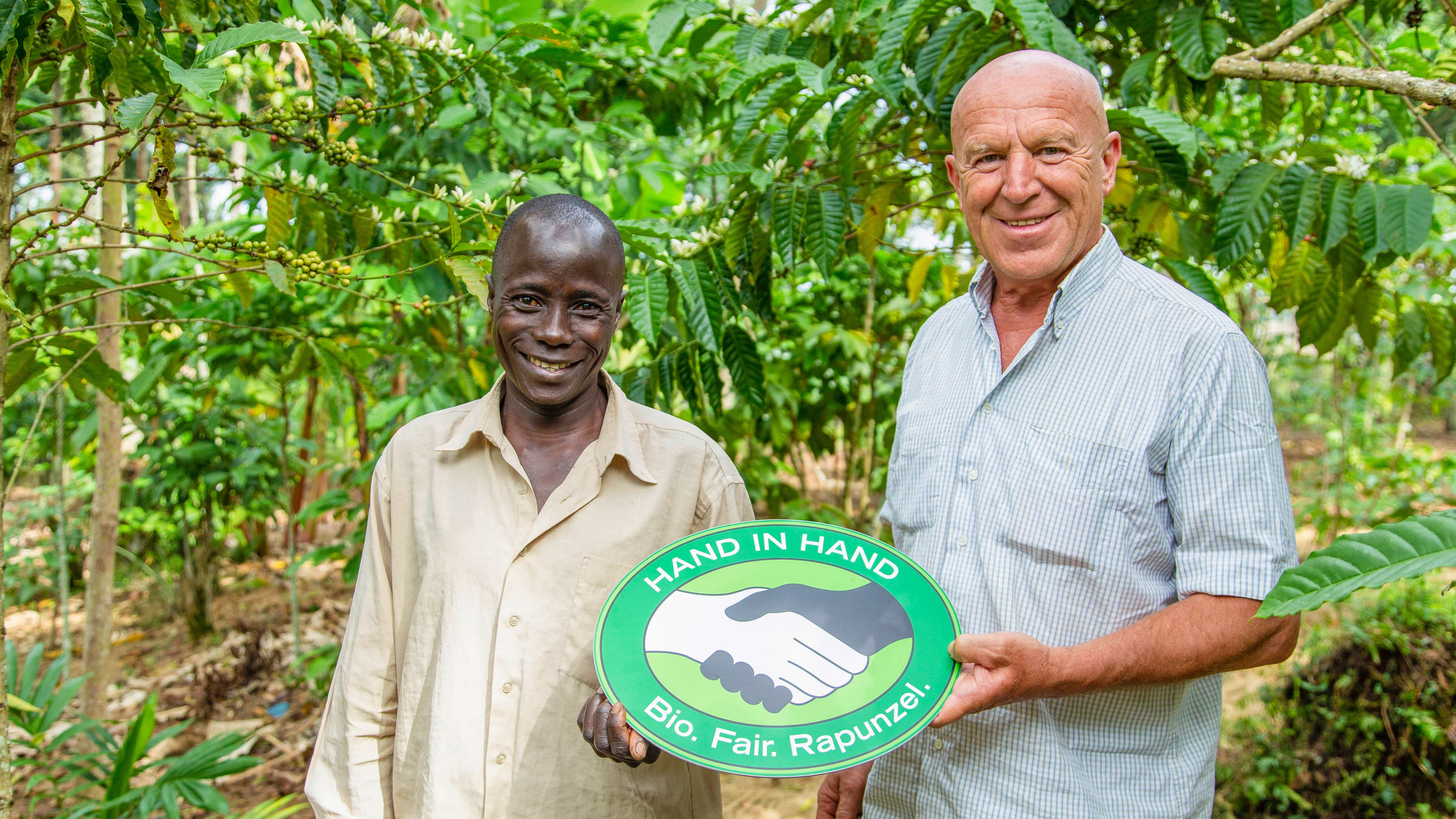 Zwei Männer stehen in einem Anbaugebiet und halten das Lgog für das Rapunzel-Konzept "Hand in Hand" in den Händen.