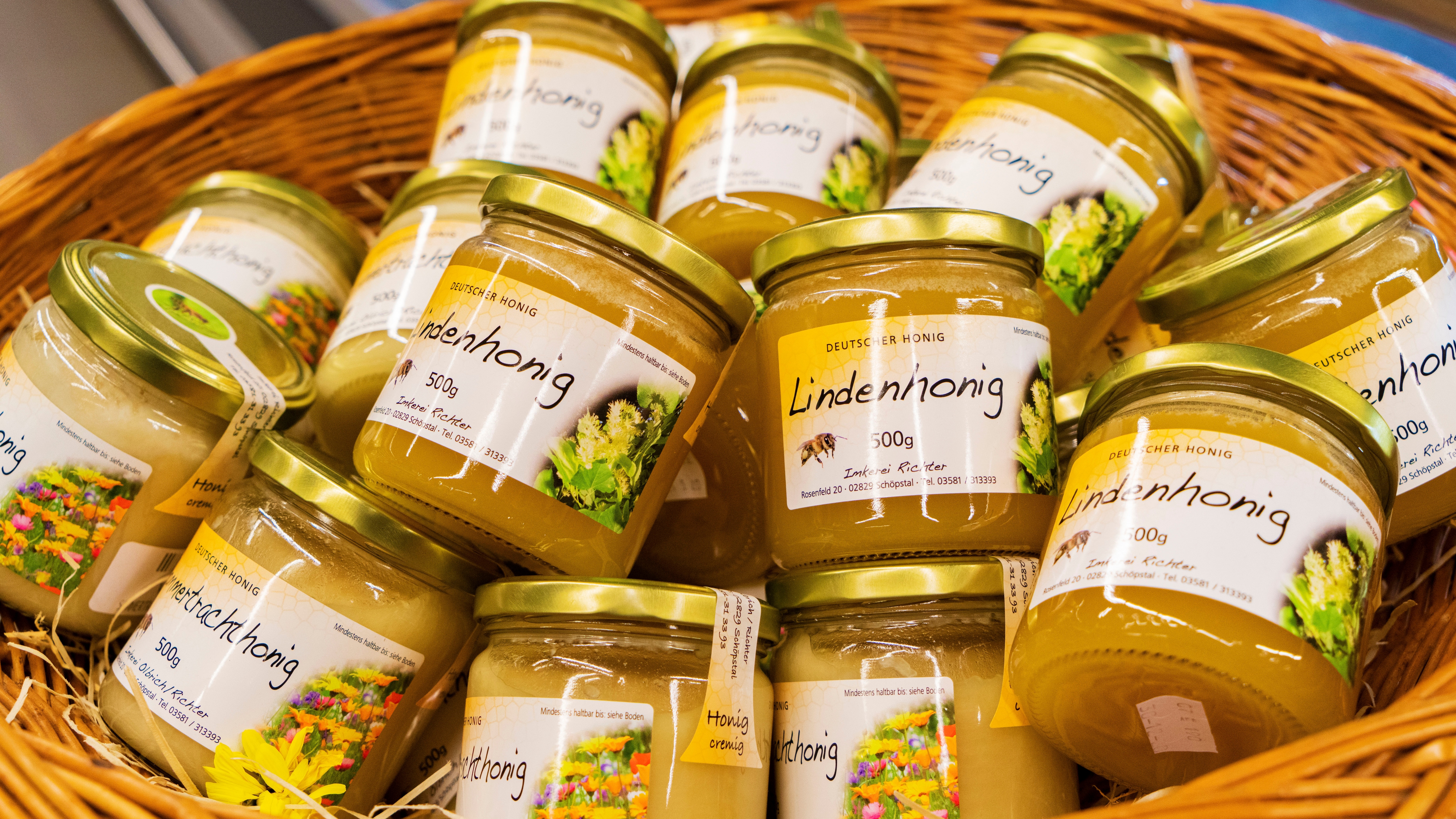 Mehrere Gläser Lindenhonig in einem geflochtenen Korb.